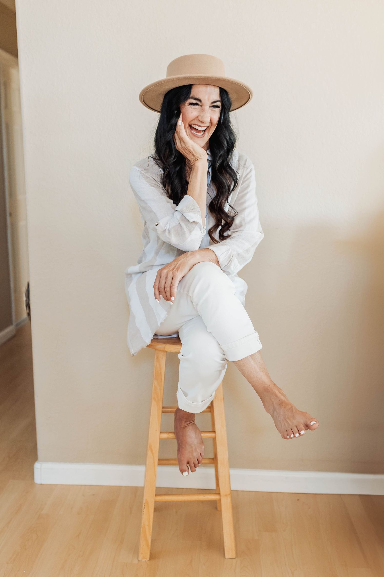 Casual lifestyle portrait of a woman in all white sitting on a wooden stool.