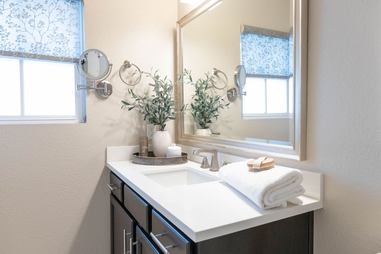 Bright bathroom vanity with white countertop, dark cabinets, and decorative greenery.