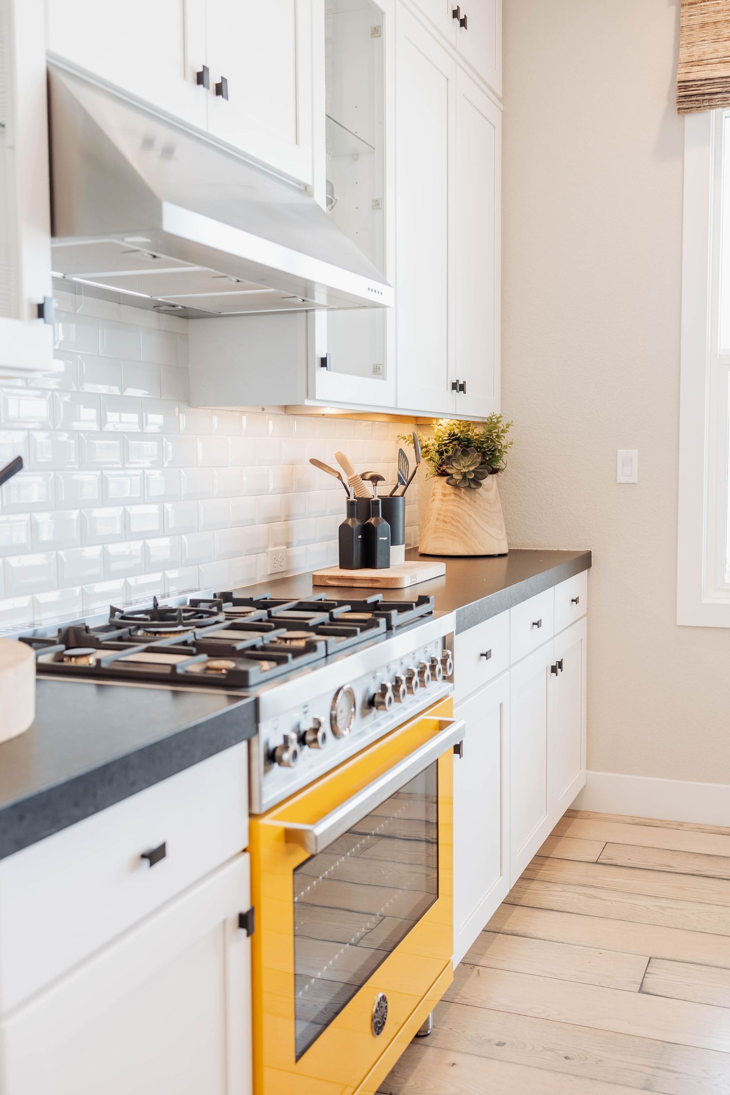 Modern white kitchen with yellow accent range and light wood flooring.