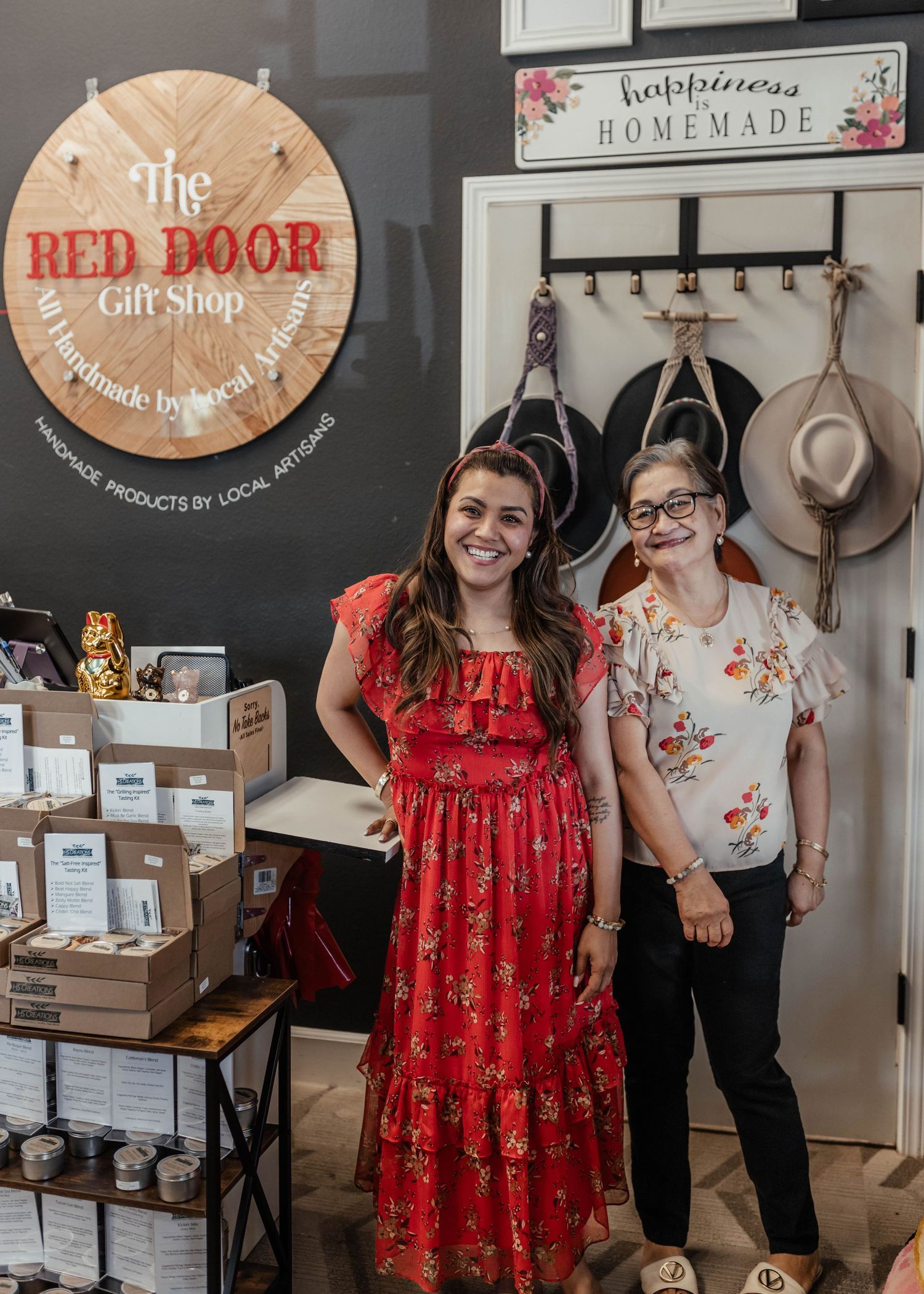 Two people pose in front of The Red Door Gift Shop's logo and product displays.