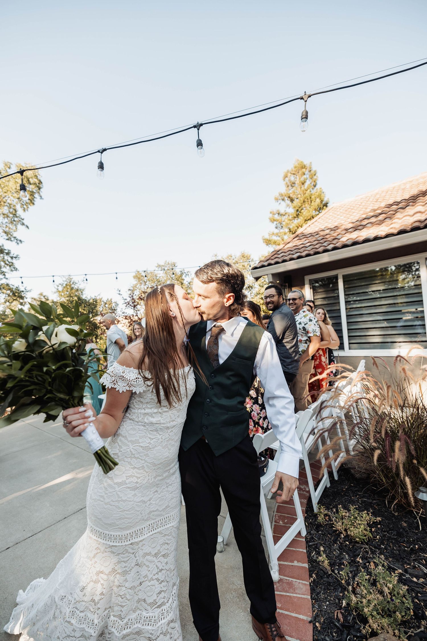 Wedding couple celebrating with guests at an outdoor reception with string lights overhead.