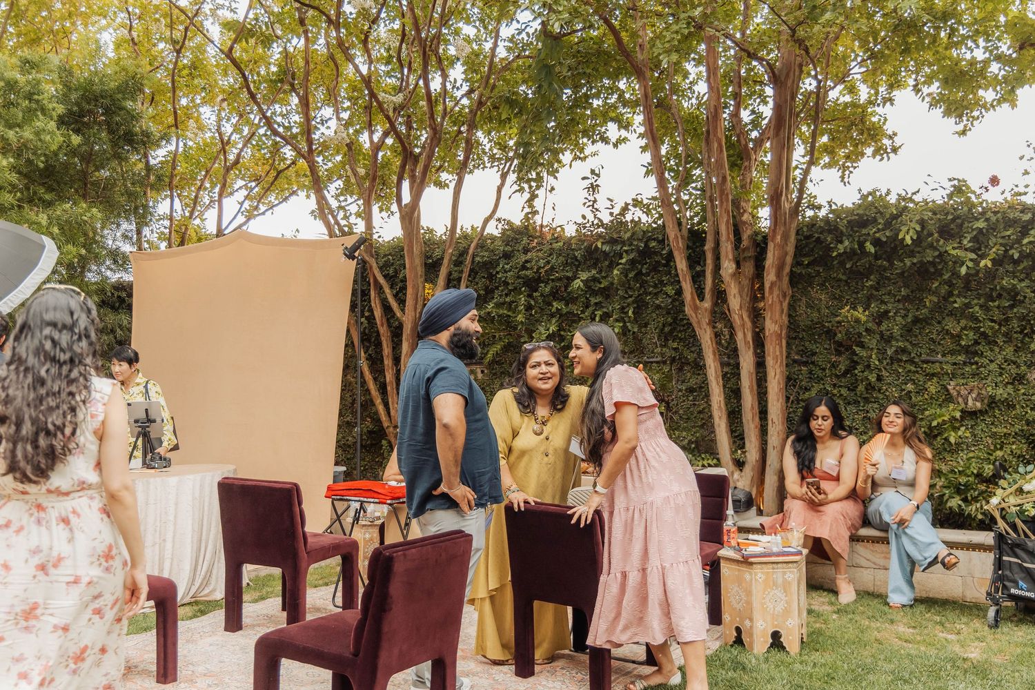 Group of guests socializing outdoors at a garden celebration with chairs and decorative backdrop.