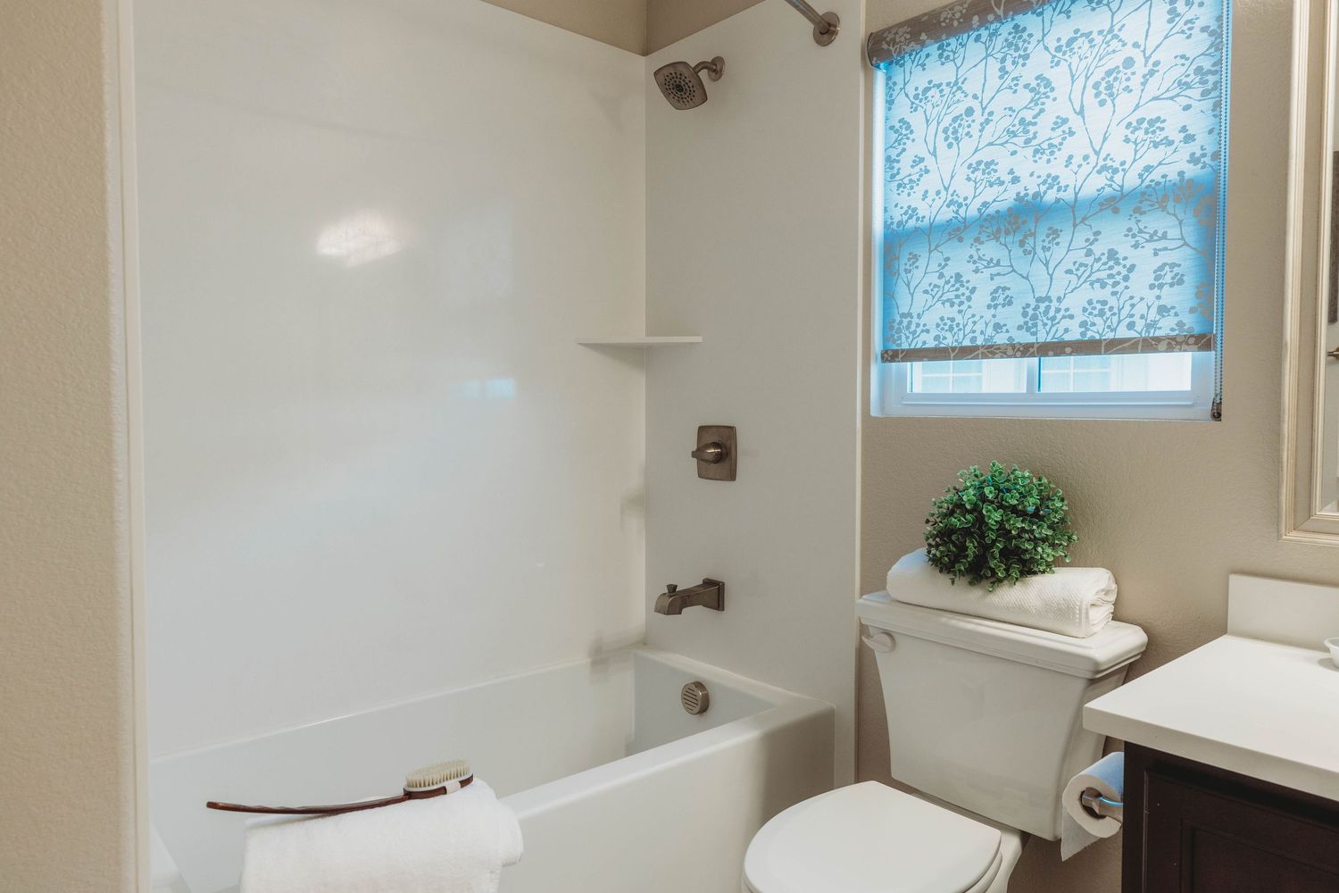 Clean white bathroom with blue patterned window shade and standard tub-shower combination.
