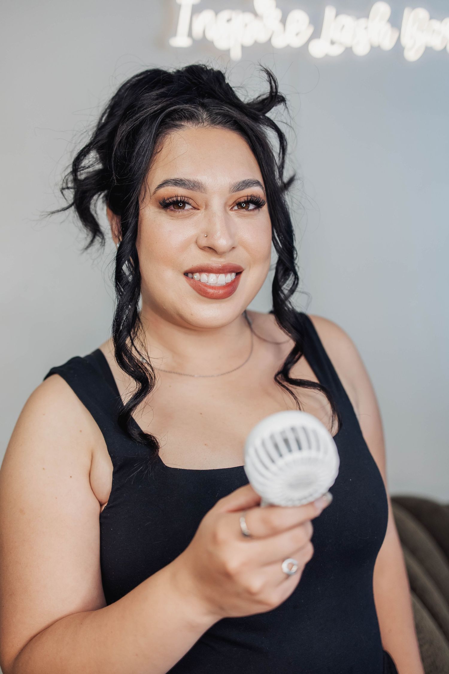 Person in black tank top holding white handheld device while smiling.