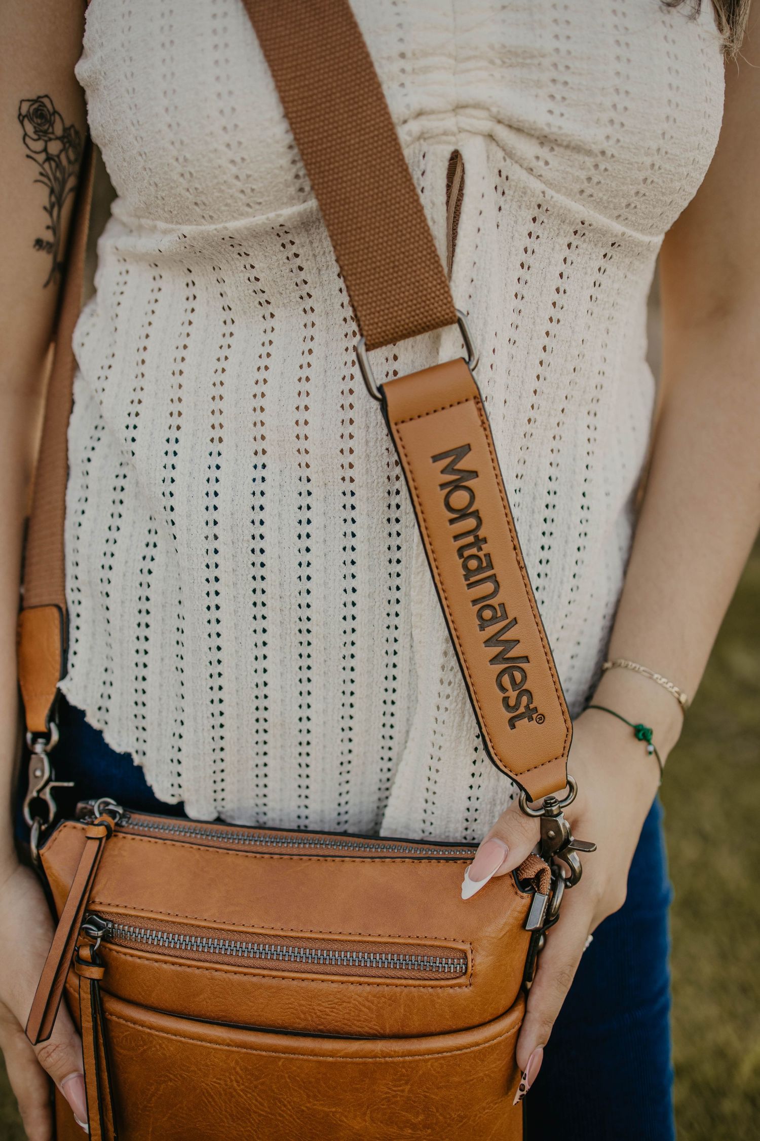Montana West branded brown leather crossbody bag shown against white eyelet fabric.