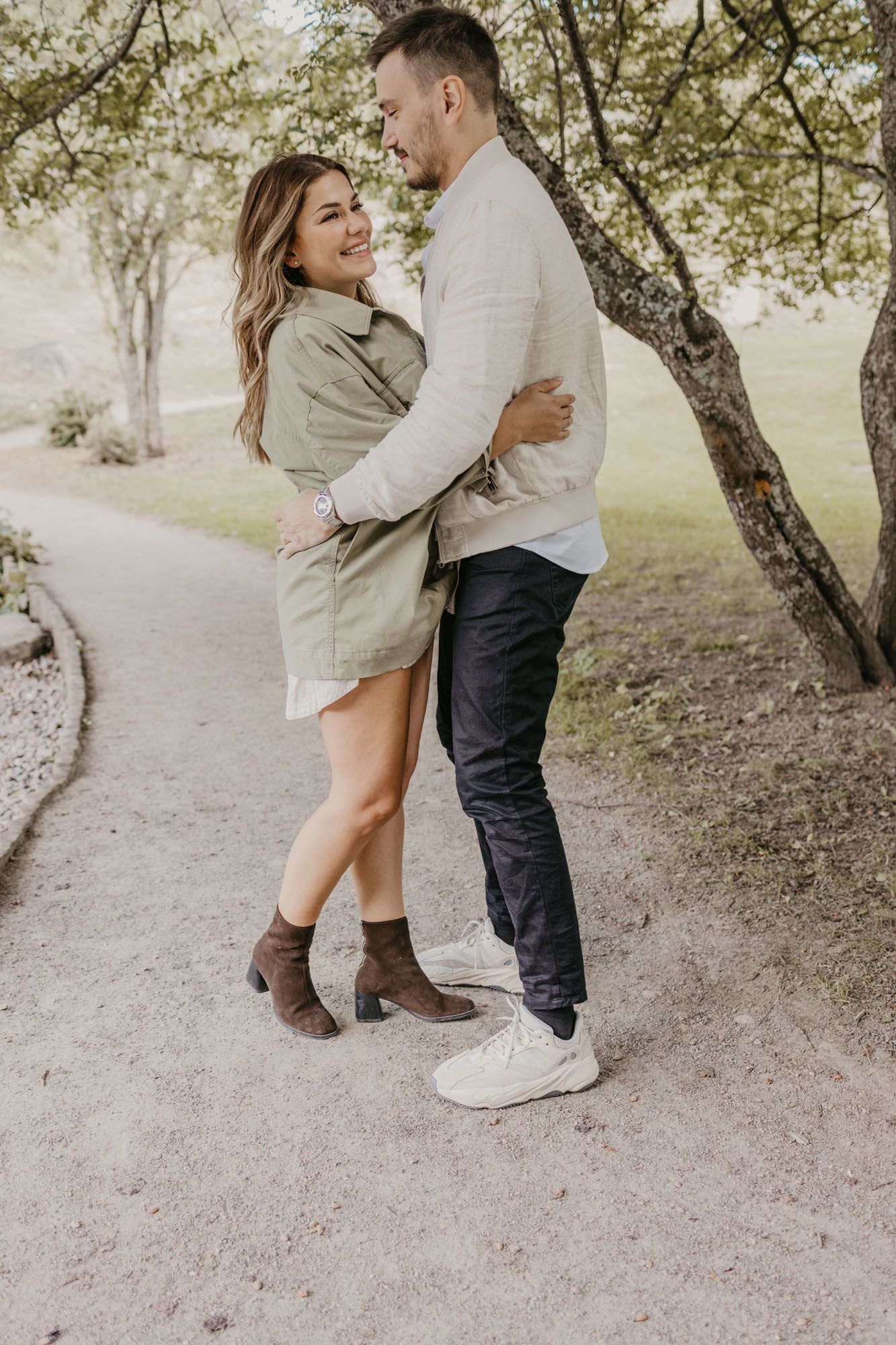 A couple shares a joyful embrace while standing on a path under blooming trees.