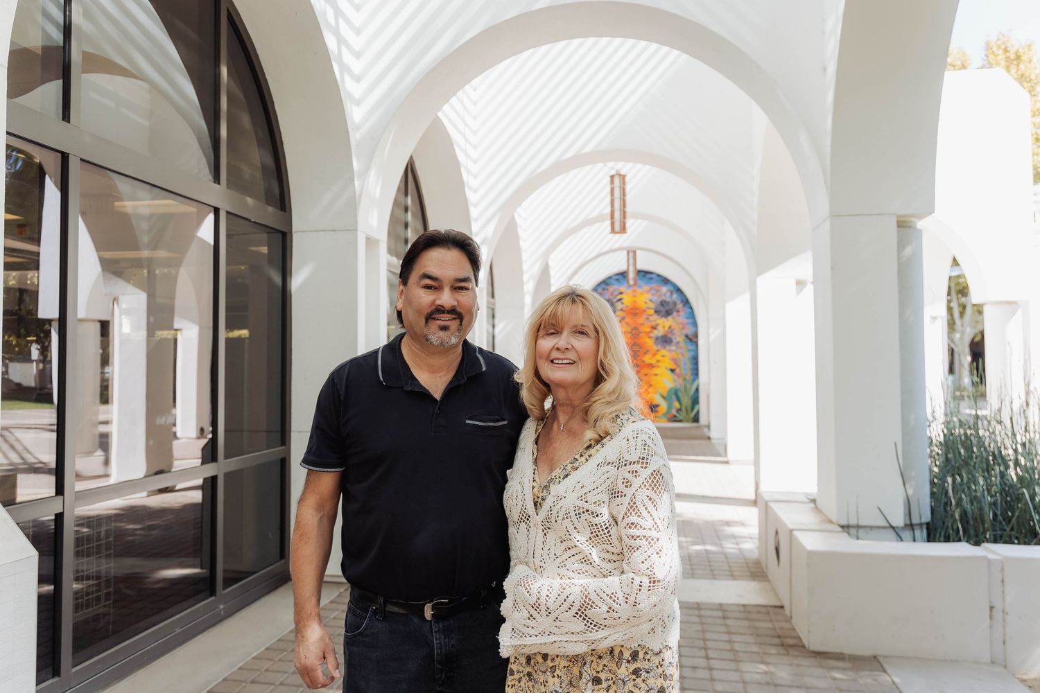 Two people standing together under white arched walkway with decorative details.