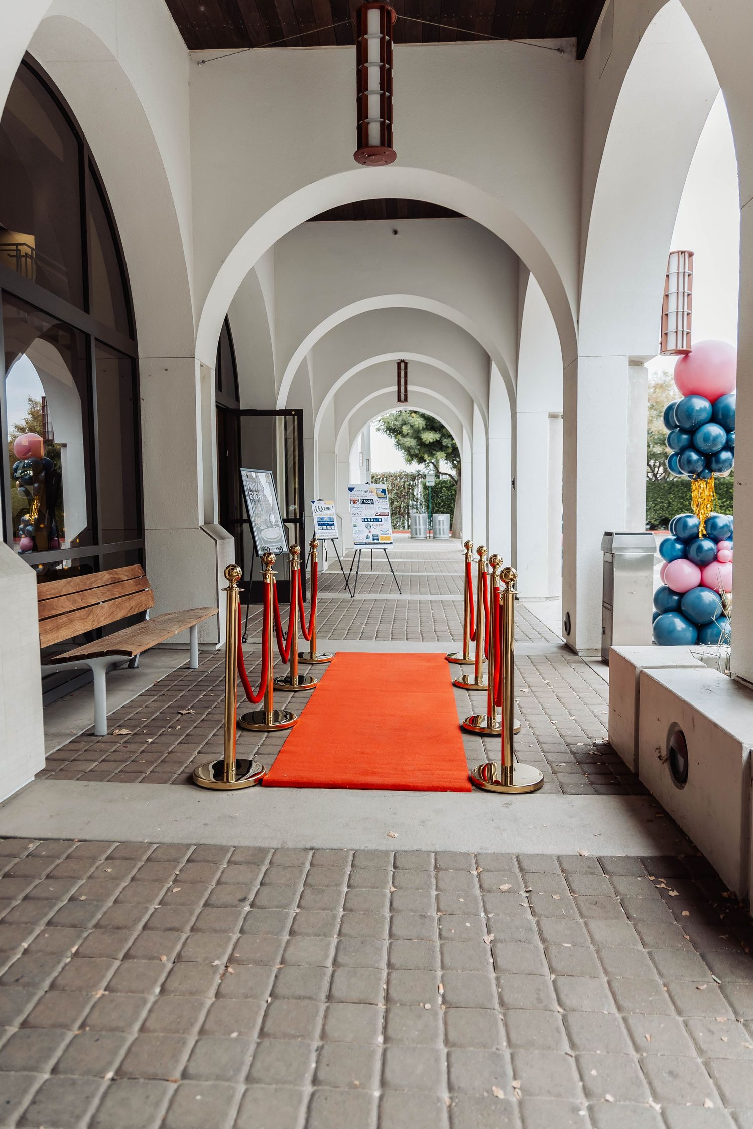 Arched colonnade walkway with red carpet and balloon decorations at the end.