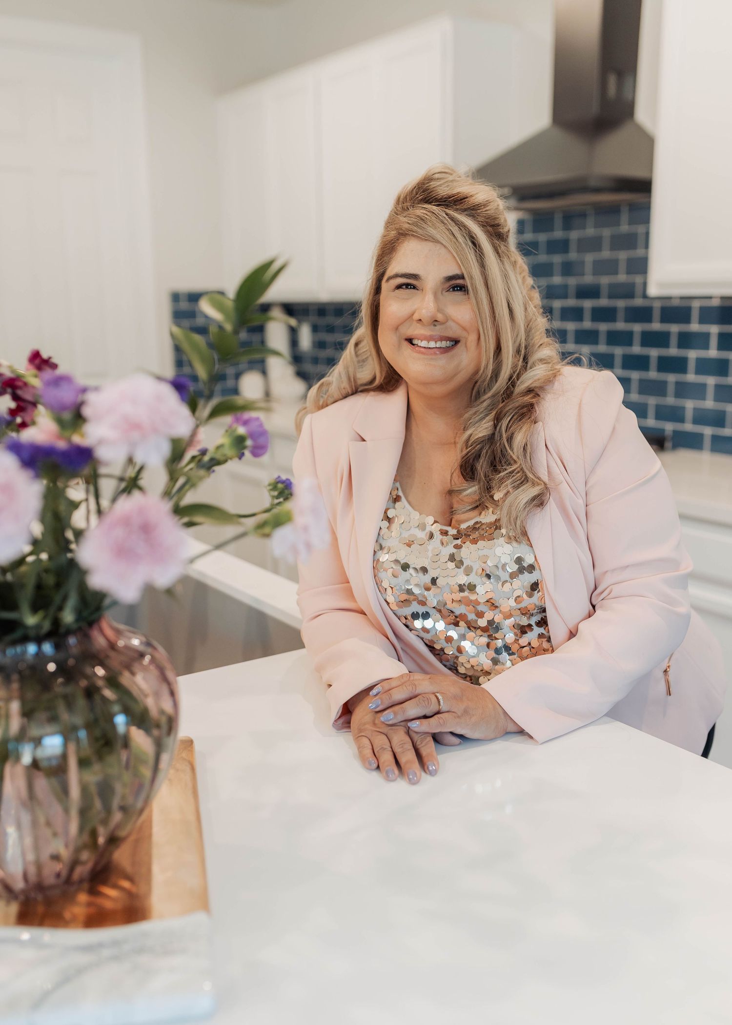 Person in pink blazer and floral top poses at modern indoor setting with orchids.