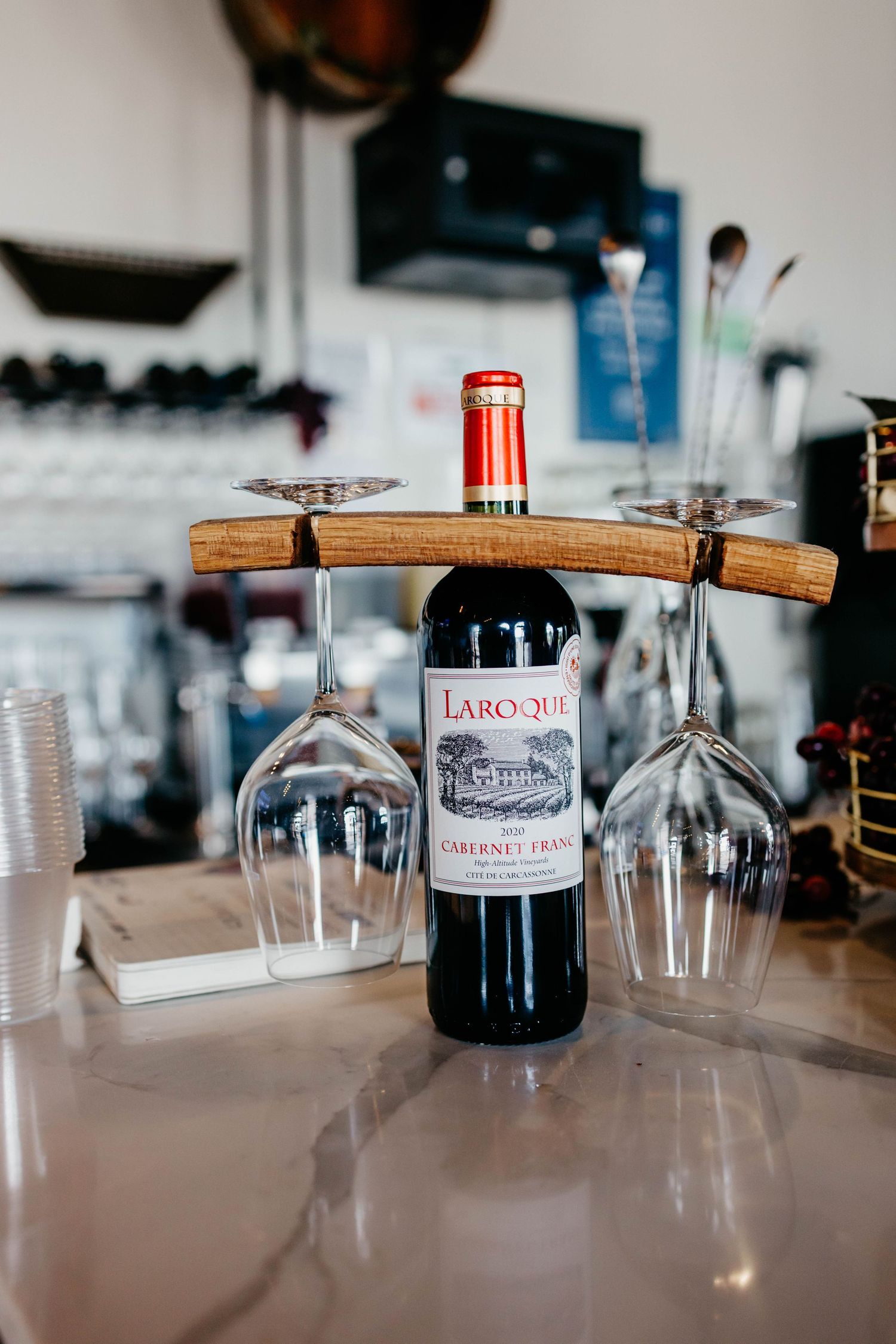 Row of wine bottles and glassware arranged on a wooden counter at a bar.