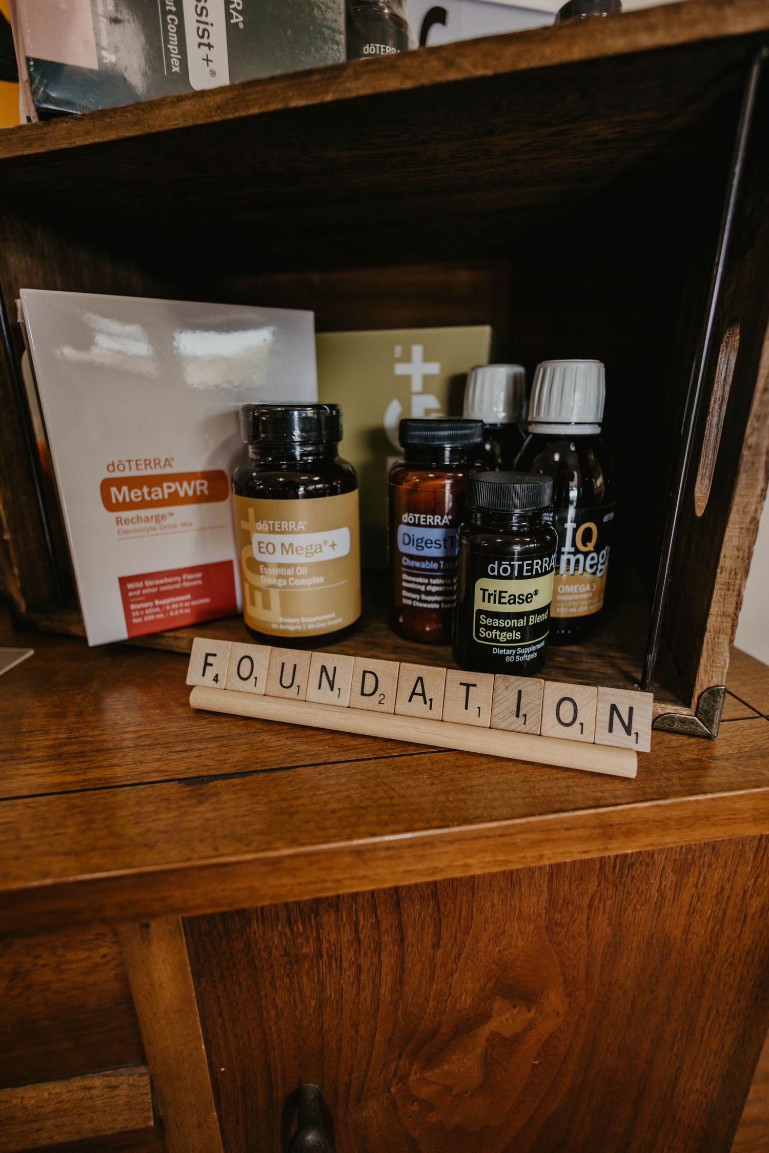 Wooden shelf displaying various wellness products and Scrabble tiles spelling 'FOUNDATION'.