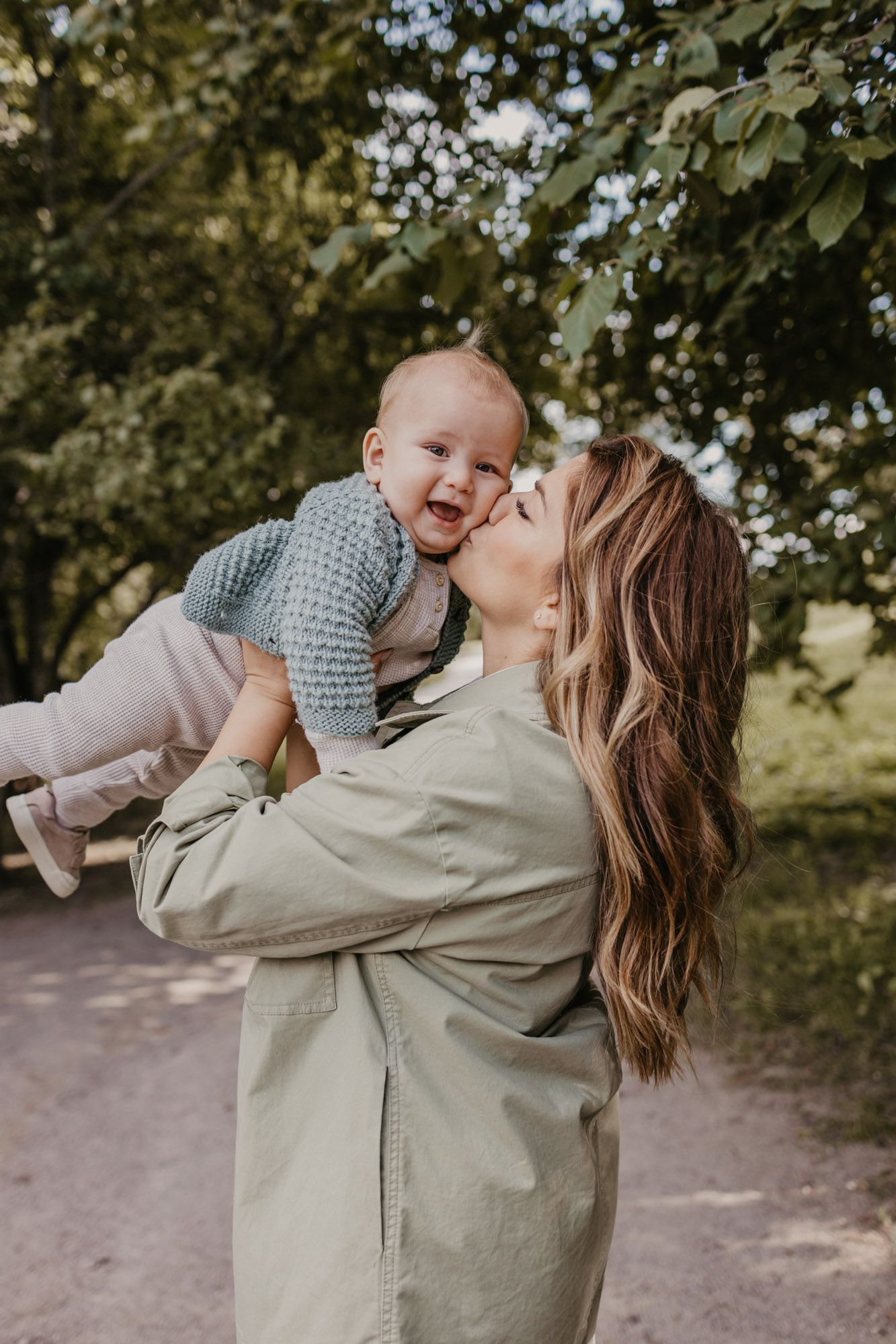 Joyful outdoor portrait showing affectionate moment between parent and baby in gray sweater.
