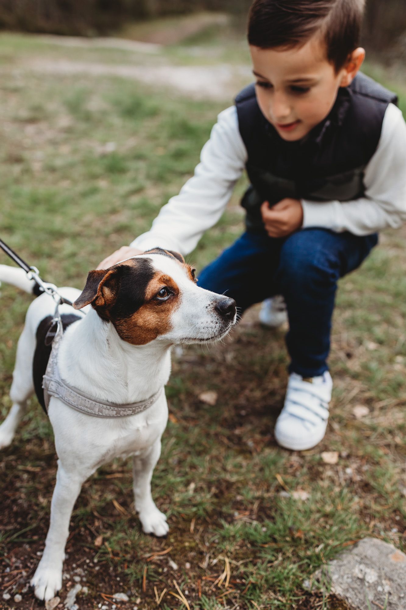 Young child crouching next to Jack Russell terrier mix dog on leash outdoors.