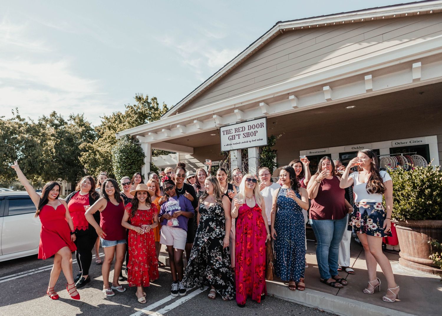 Group poses together outside a retail storefront wearing festive red and floral dresses.