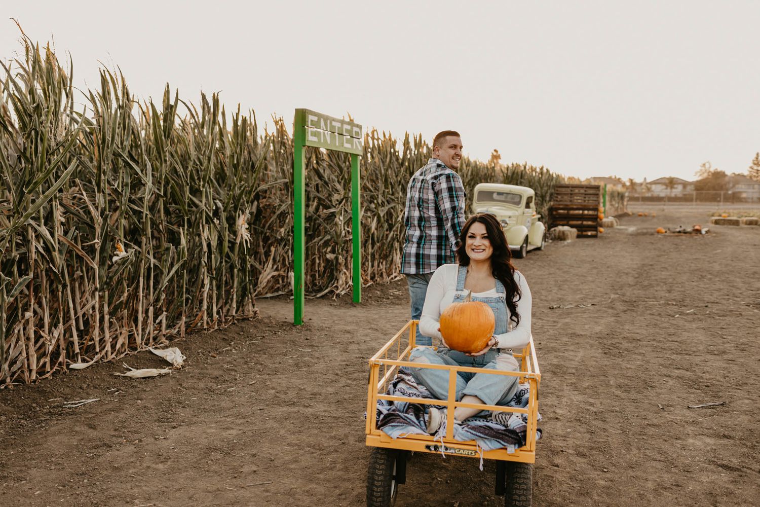 A couple enjoy a romantic moment in a wooden wagon next to a cornfield during golden hour.