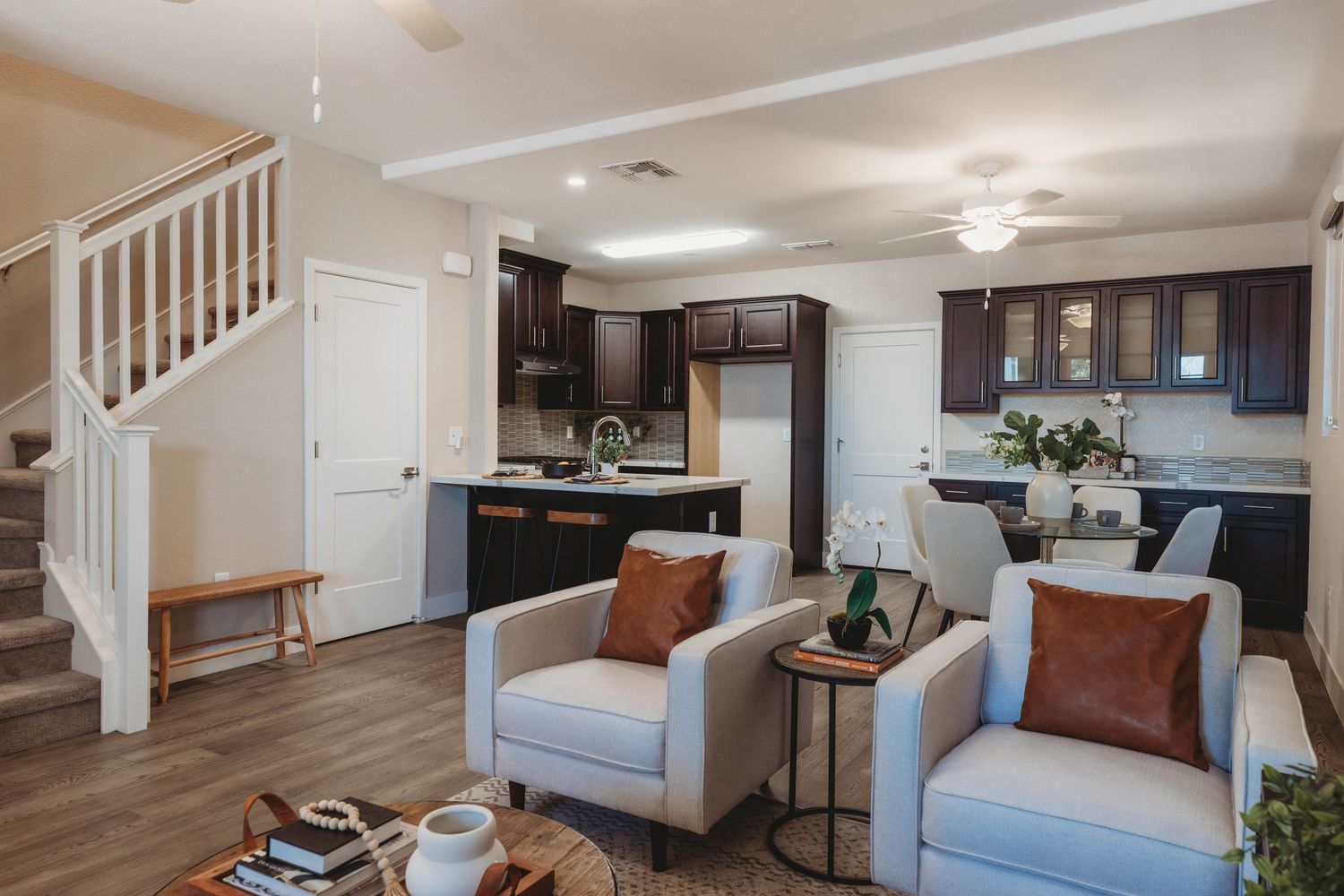 Living room featuring light blue accent chairs, dark wood cabinets, and white staircase railings.