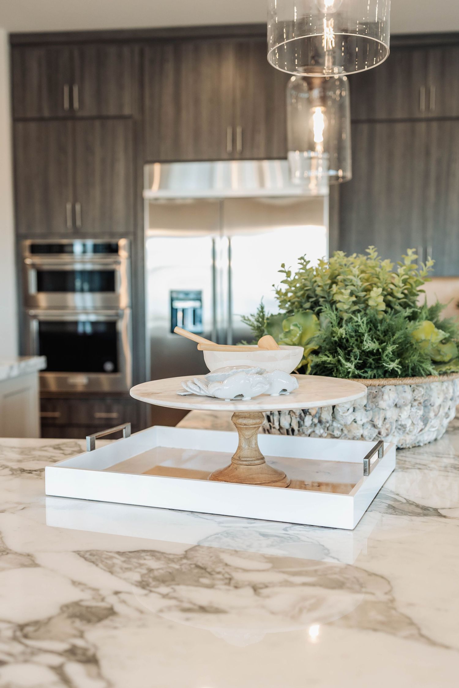Modern kitchen island with marble countertops, stainless appliances, and decorative greenery in a bright open space.
