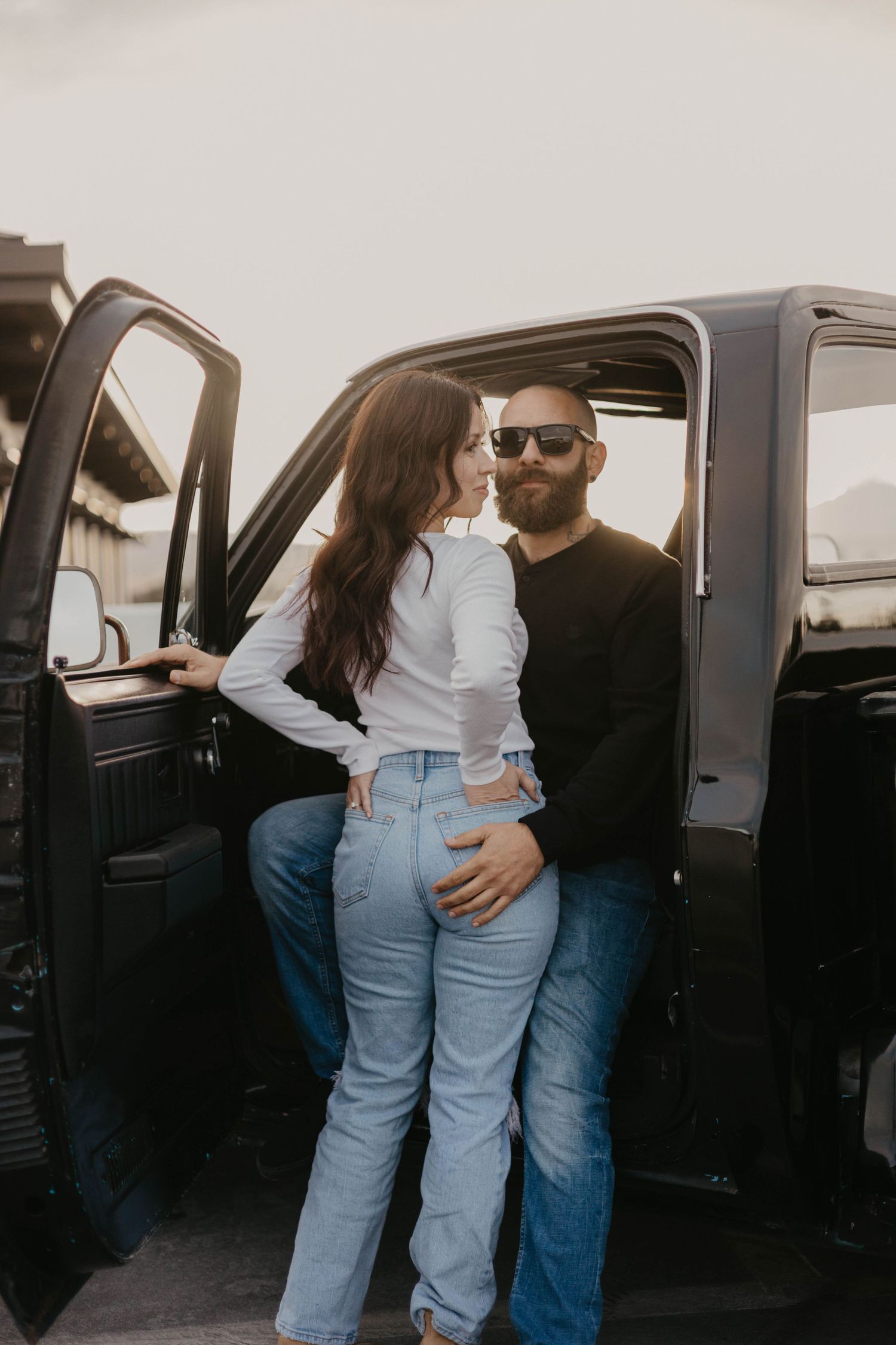 Couple sharing tender moments near a parked vehicle during casual photoshoot.