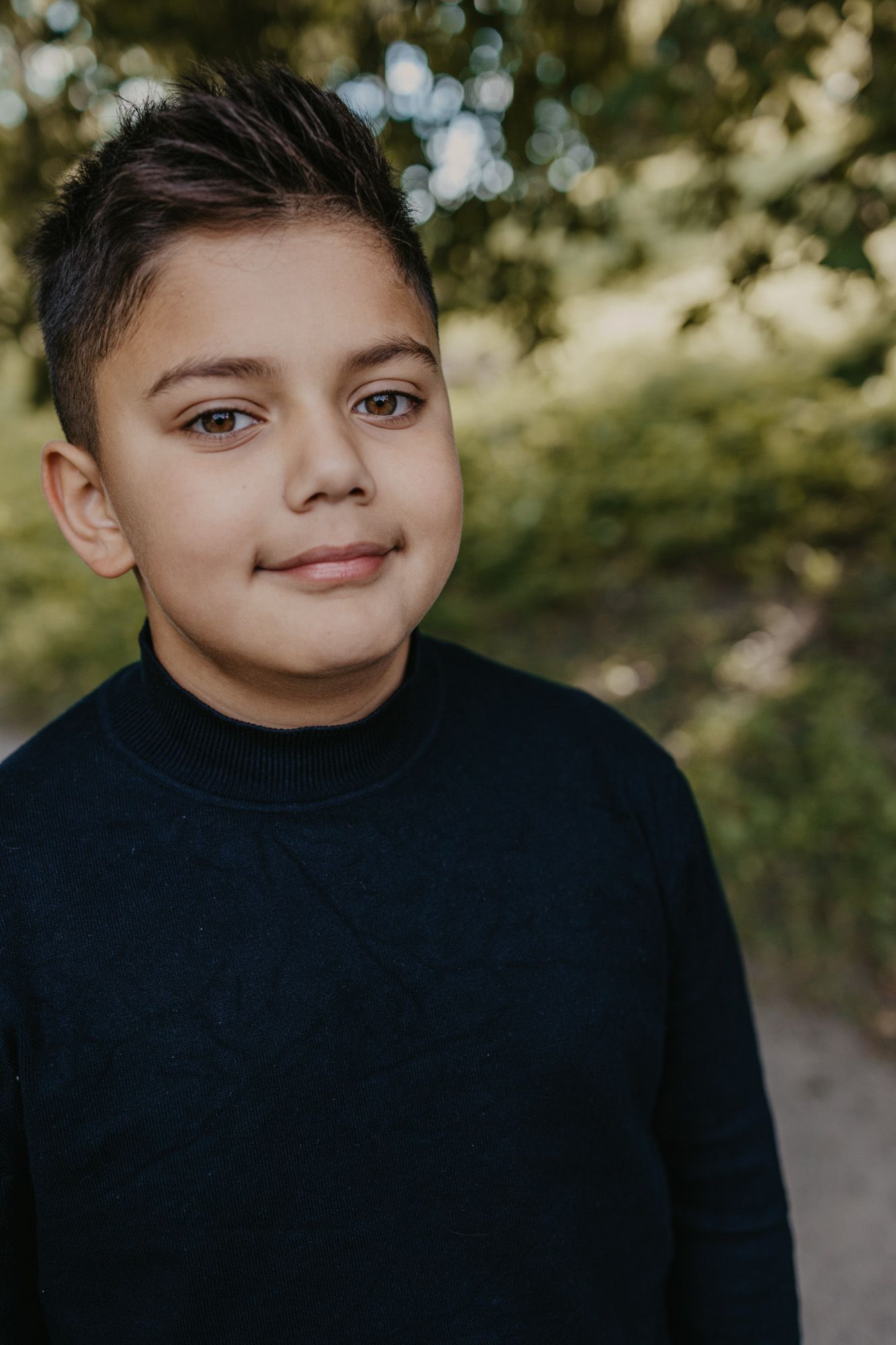 Portrait of young boy in black sweater smiling against blurred natural background.