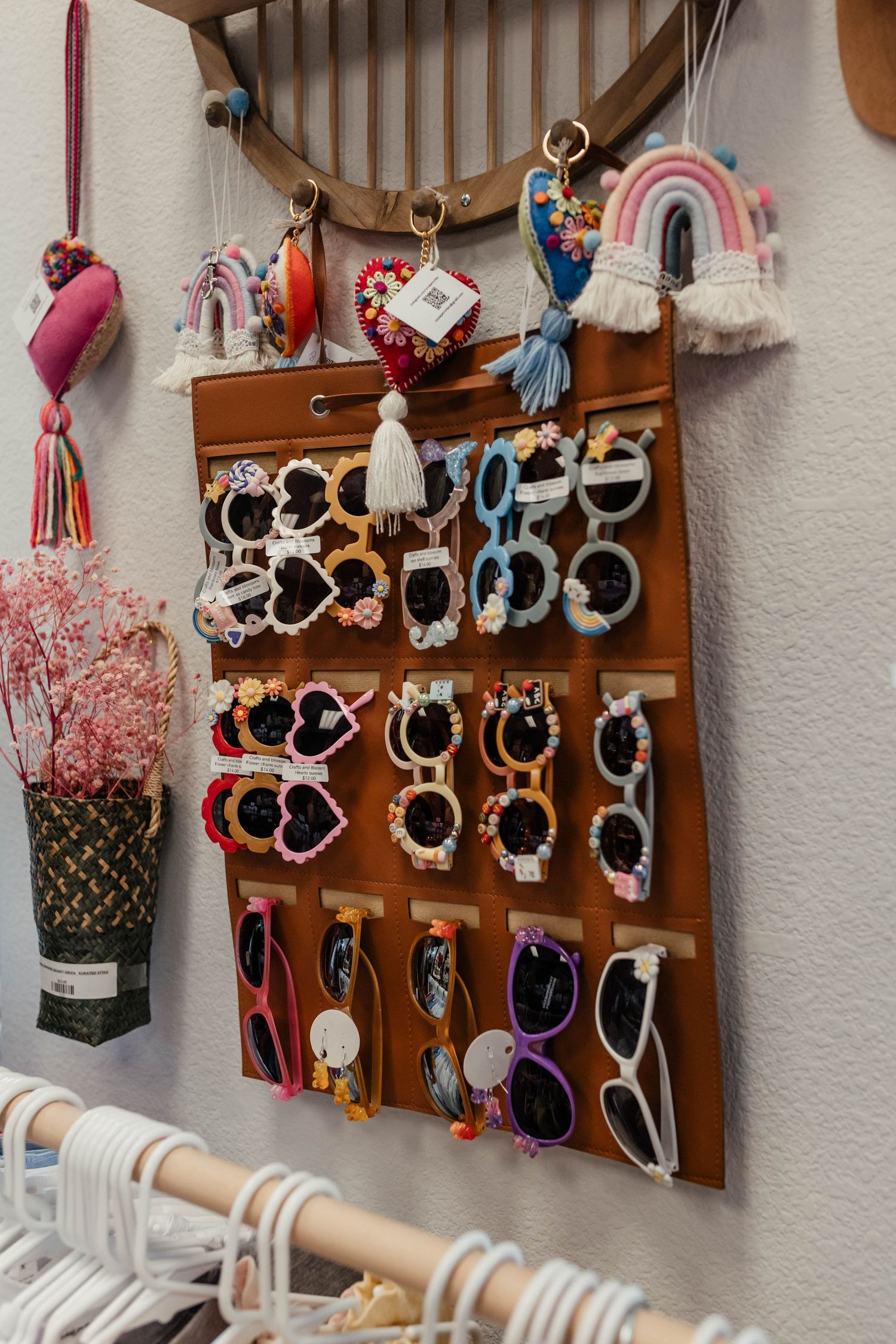 Colorful sunglasses display organizer mounted on wall with hanging rainbow and floral accessories.