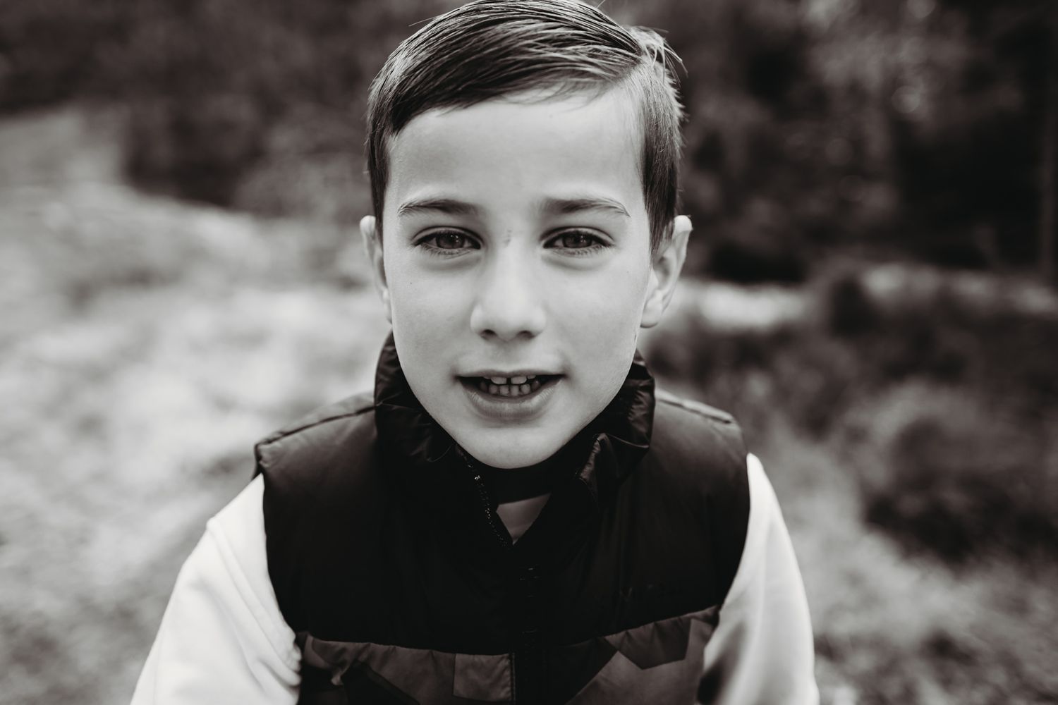 Black and white close-up portrait of young child smiling outdoors.