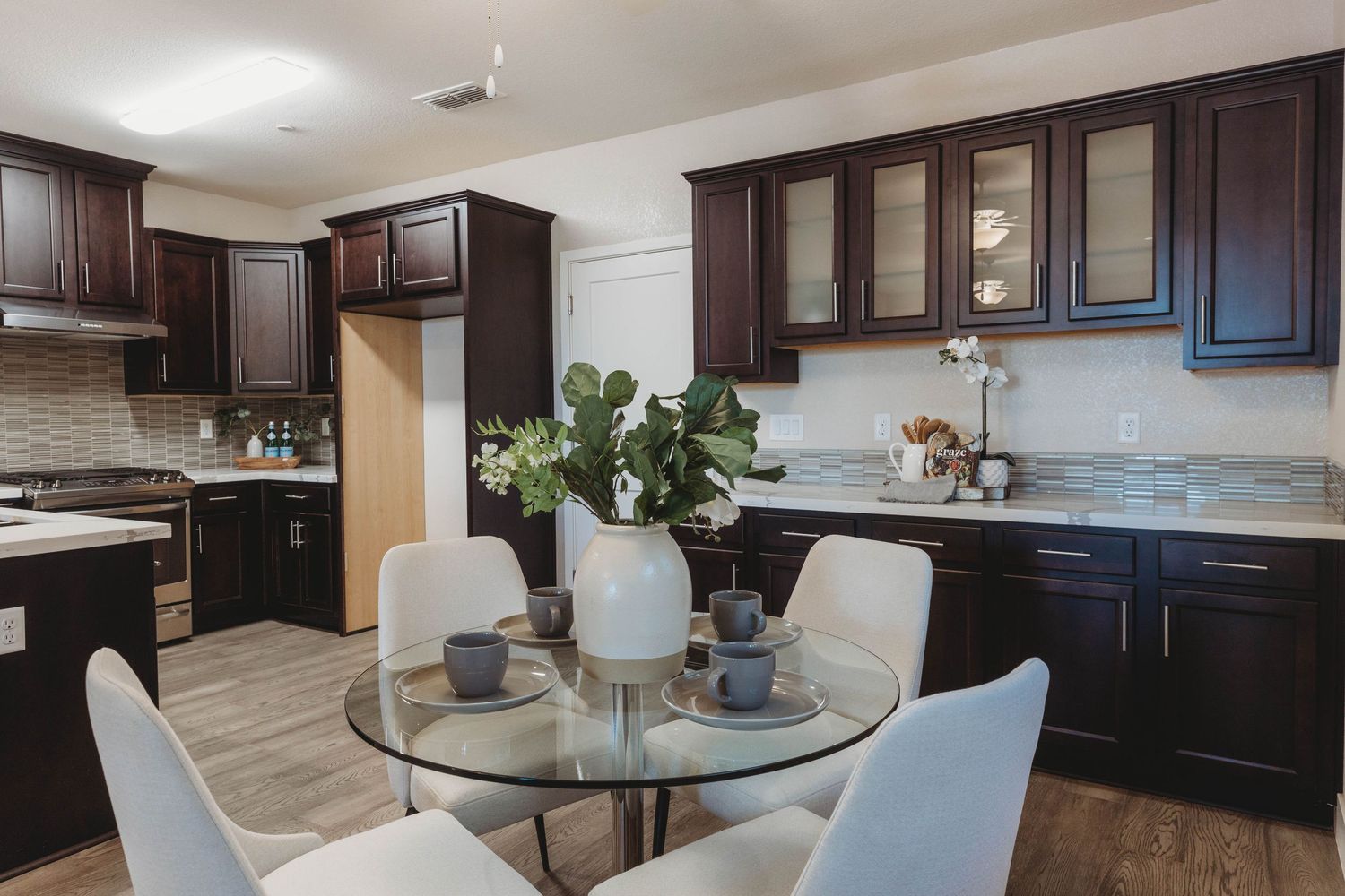 Elegant dining area with glass table, white chairs, and dark wood kitchen cabinetry.