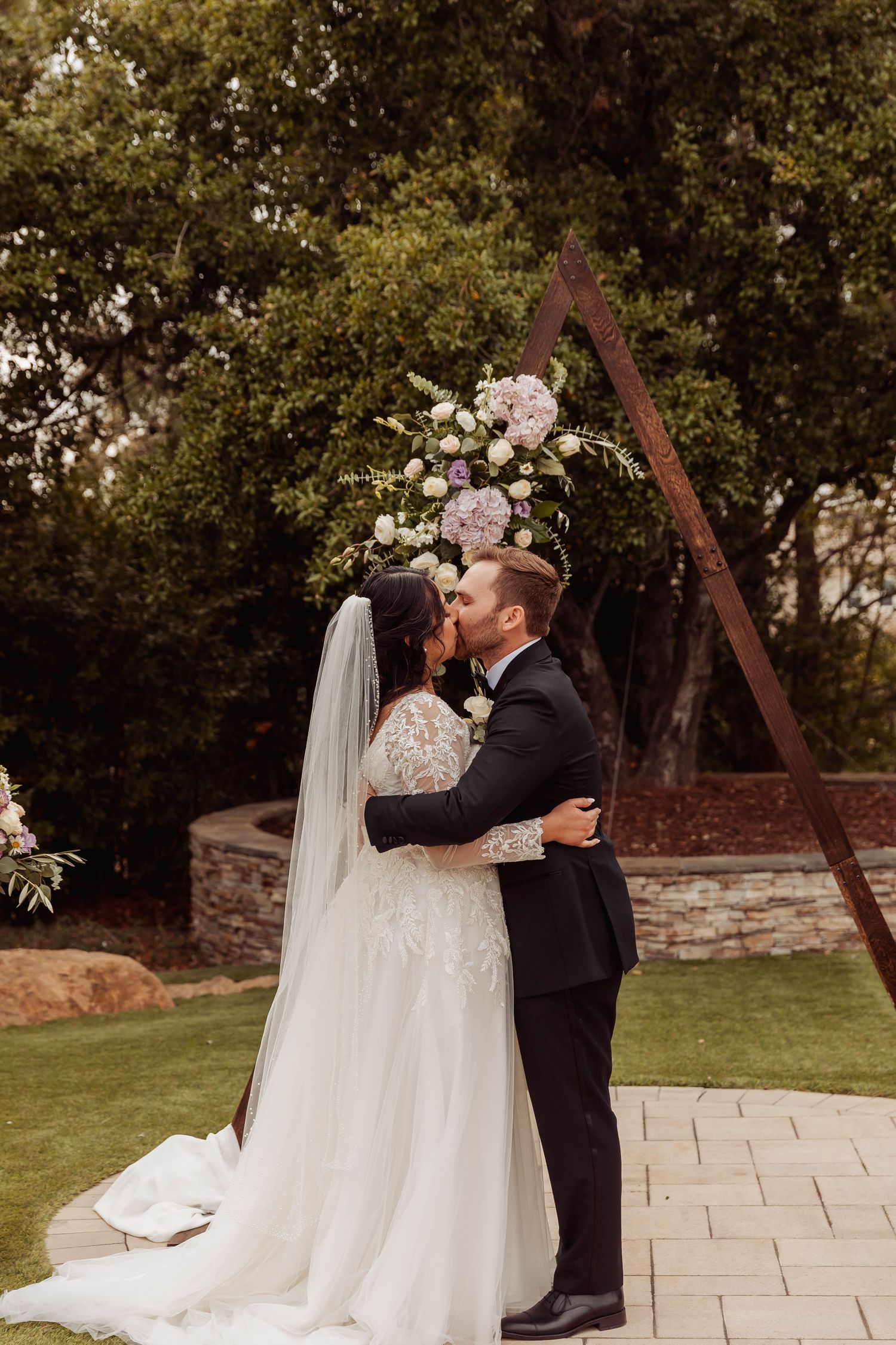 Outdoor wedding ceremony with couple embracing under trees.