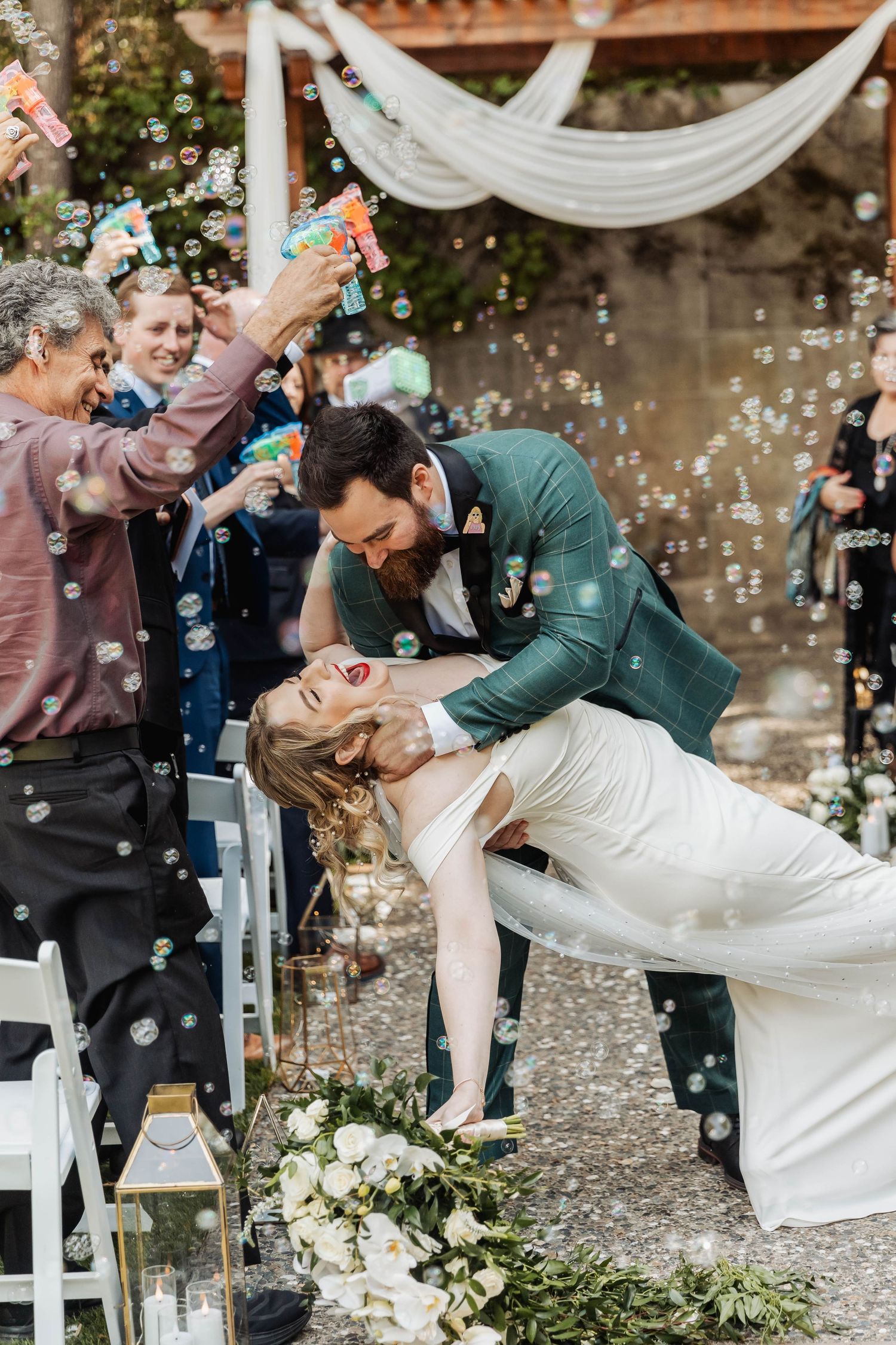 Romantic wedding ceremony moment with bubbles floating through the air as couple shares a dramatic dip kiss.