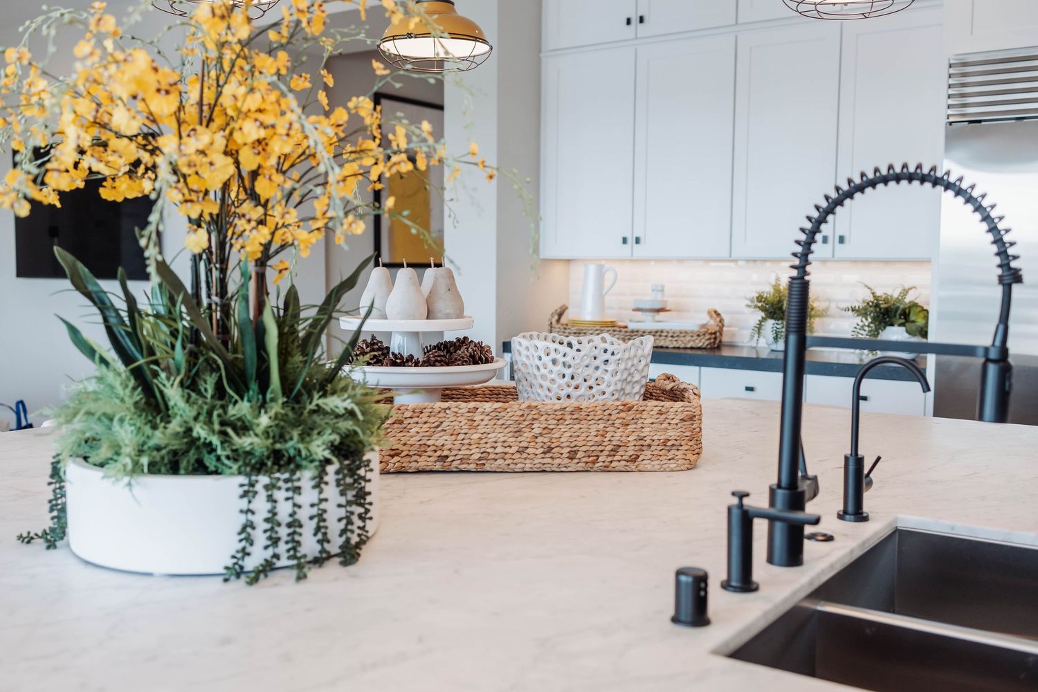 Modern white kitchen interior with pendant lights and yellow floral arrangements.