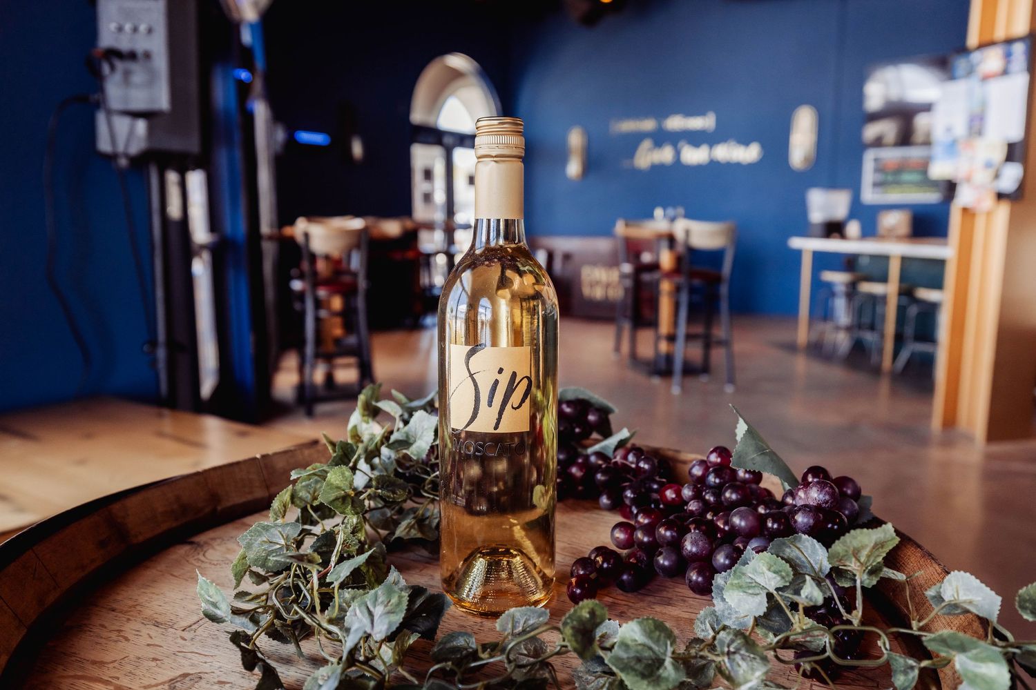 Wine bottles displayed with greenery on wooden table in restaurant setting.