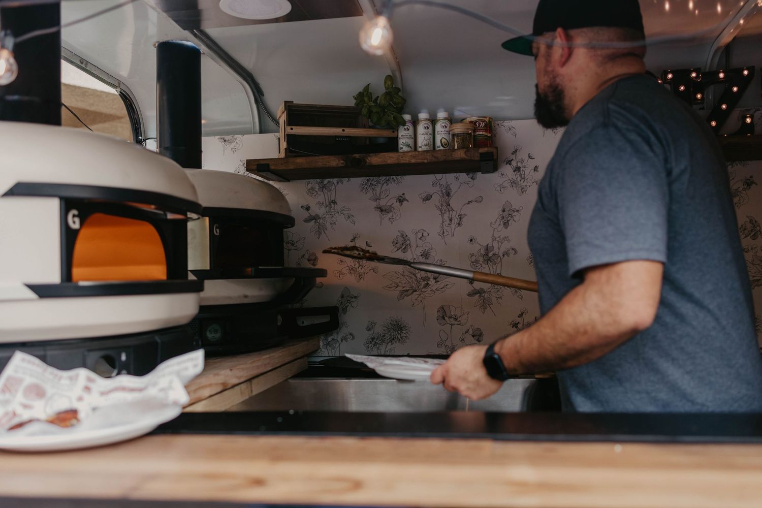 Pizza preparation station with ovens and cooking equipment in a commercial kitchen.