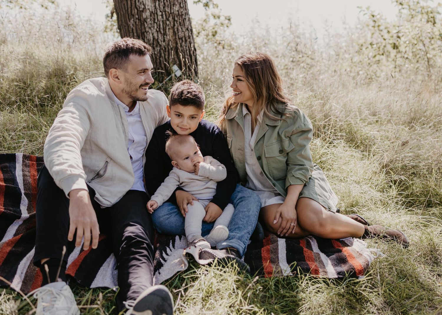 Family sharing intimate moments while sitting on a picnic blanket in nature.
