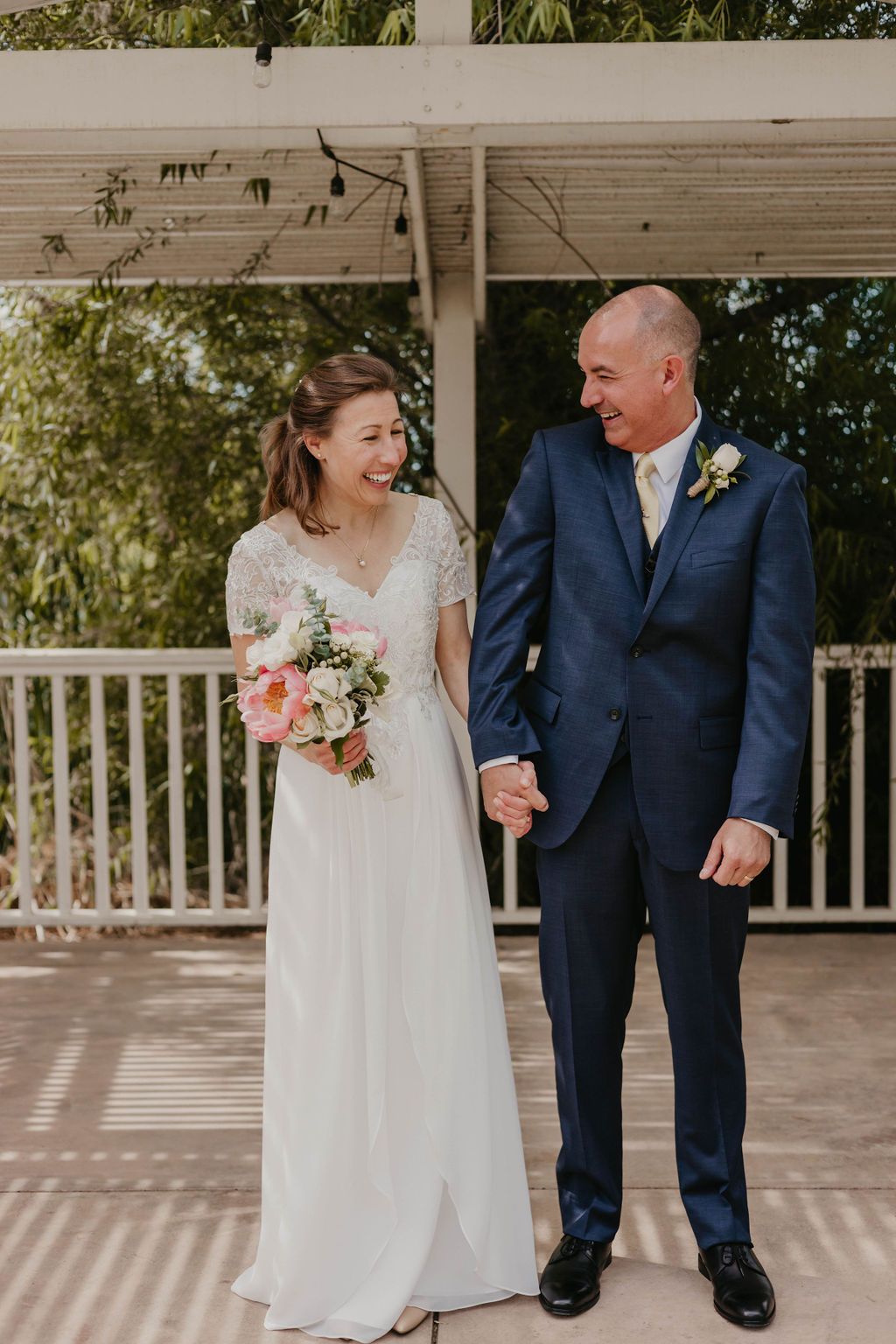Newlyweds standing together on a white porch with bride holding pink and white bouquet.