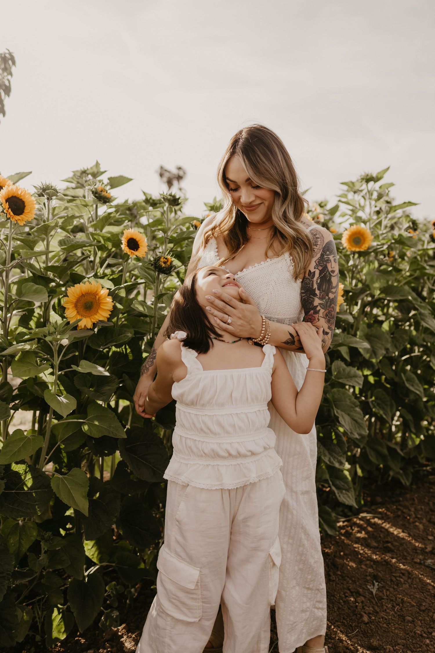 A series of intimate photographs showing two people posing together among tall sunflowers in white outfits.