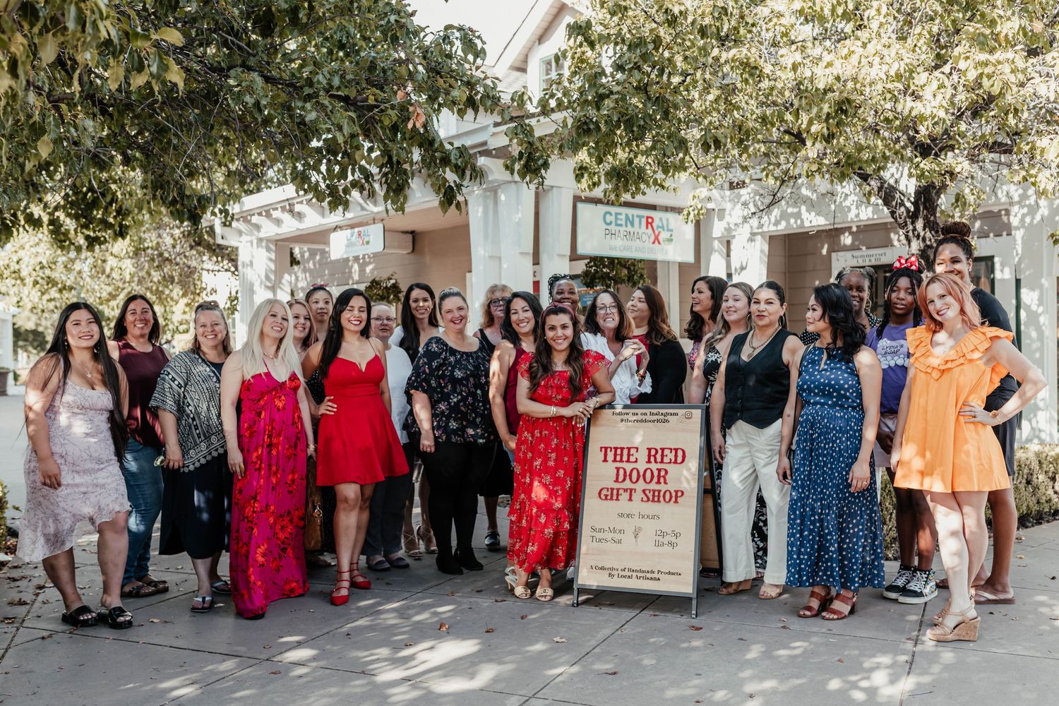 A group of women in colorful dresses pose together outside The Red Door Gift Shop.