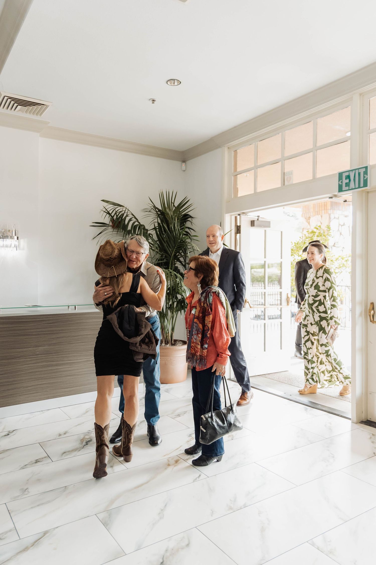 Guests greet each other in a bright, modern lobby with marble floors and a large tropical plant near the entrance.