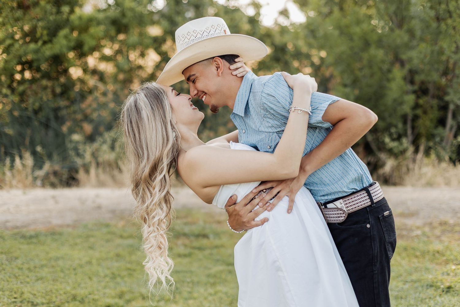 Couple in western attire sharing romantic dip pose in outdoor setting.