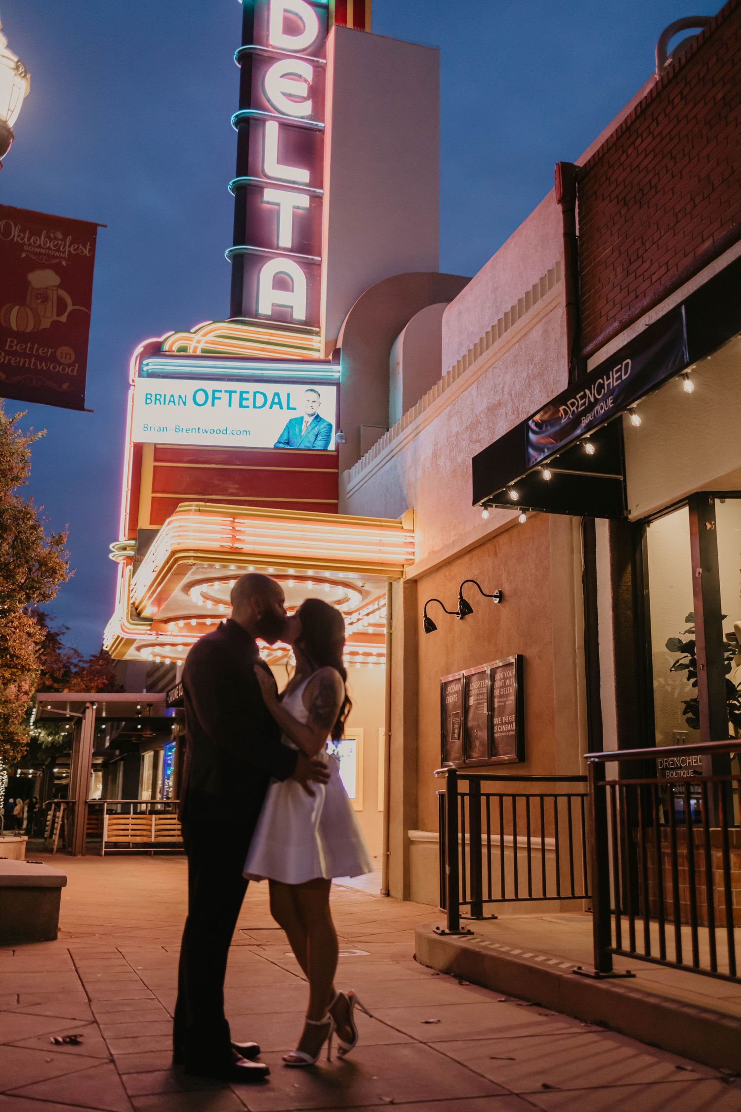 A couple sharing an intimate moment outside a vintage theater with illuminated Delta sign.