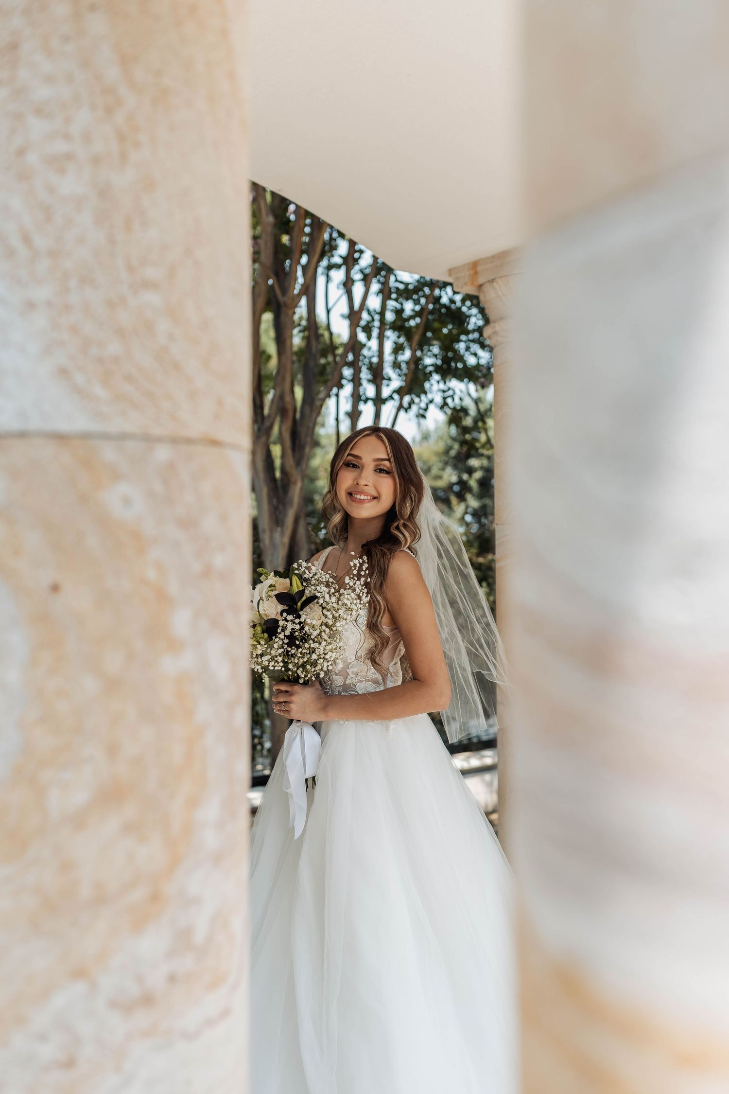 Candid bridal portrait framed by stone column with natural garden backdrop.
