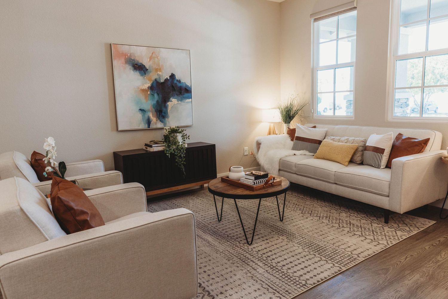Bright living room with modern furniture, abstract wall art, and natural light from windows.