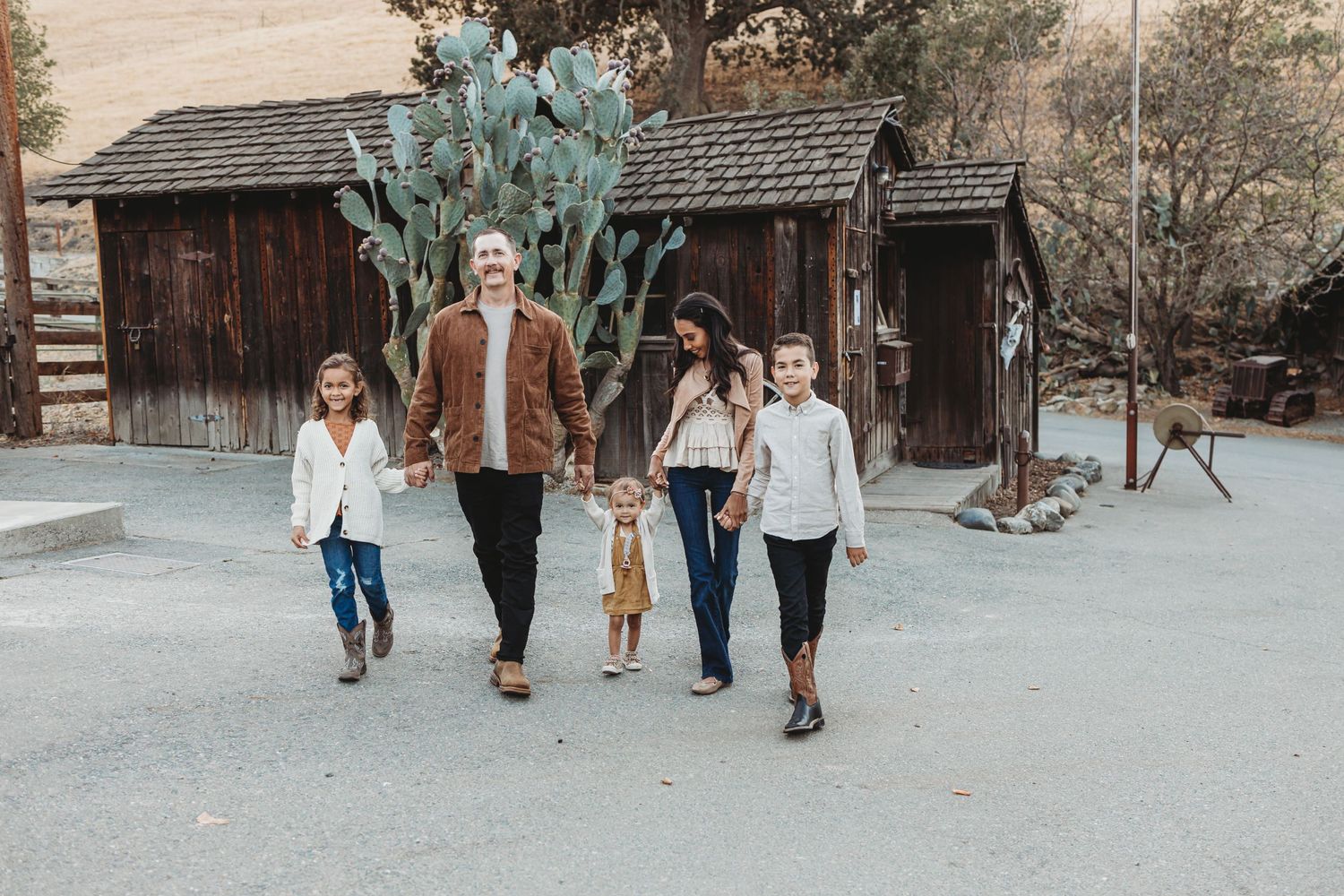 Family taking a casual stroll on path with rustic buildings and large cactus in background.