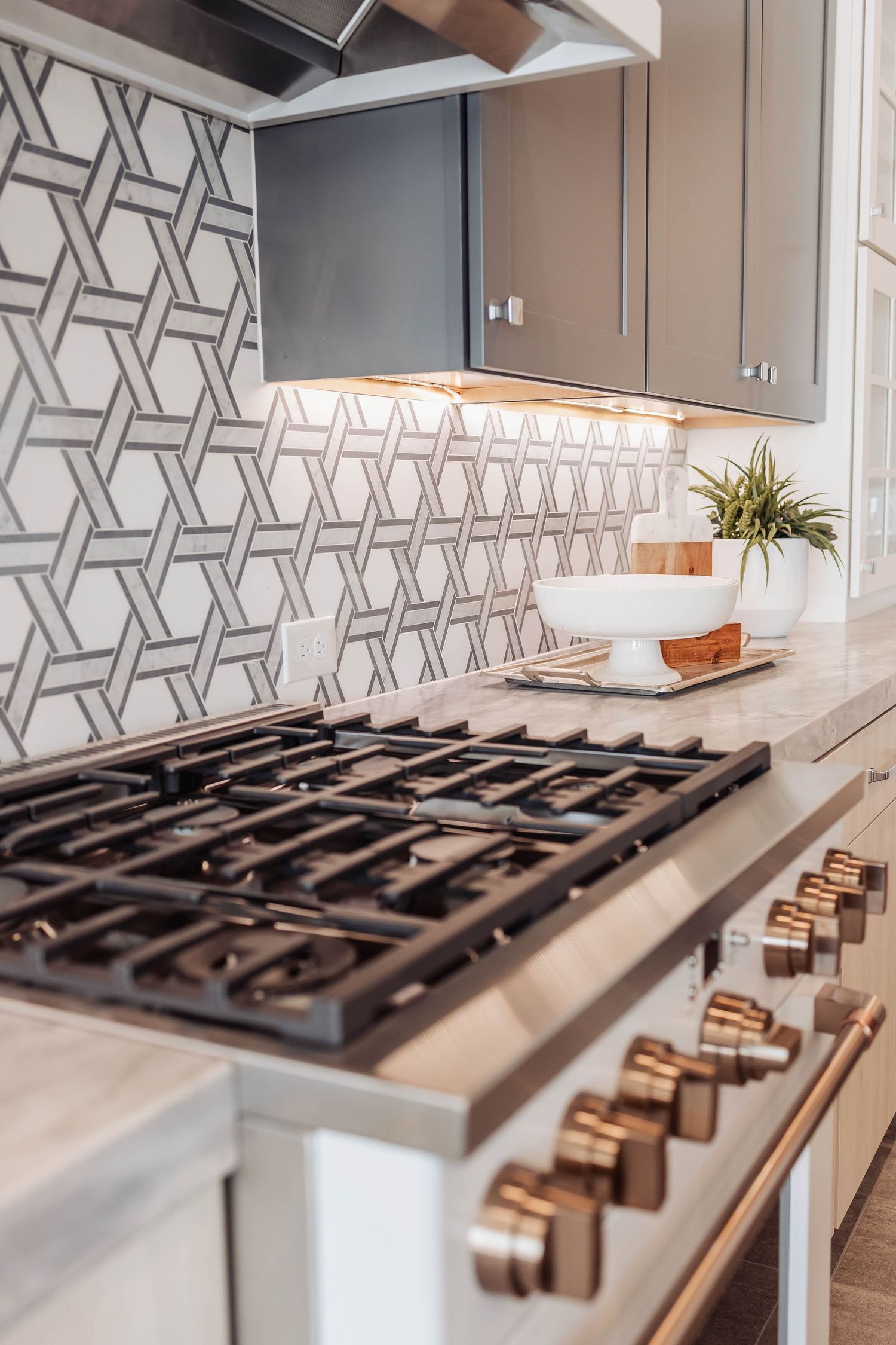Sleek gas cooktop with copper knobs and geometric backsplash in contemporary kitchen design.