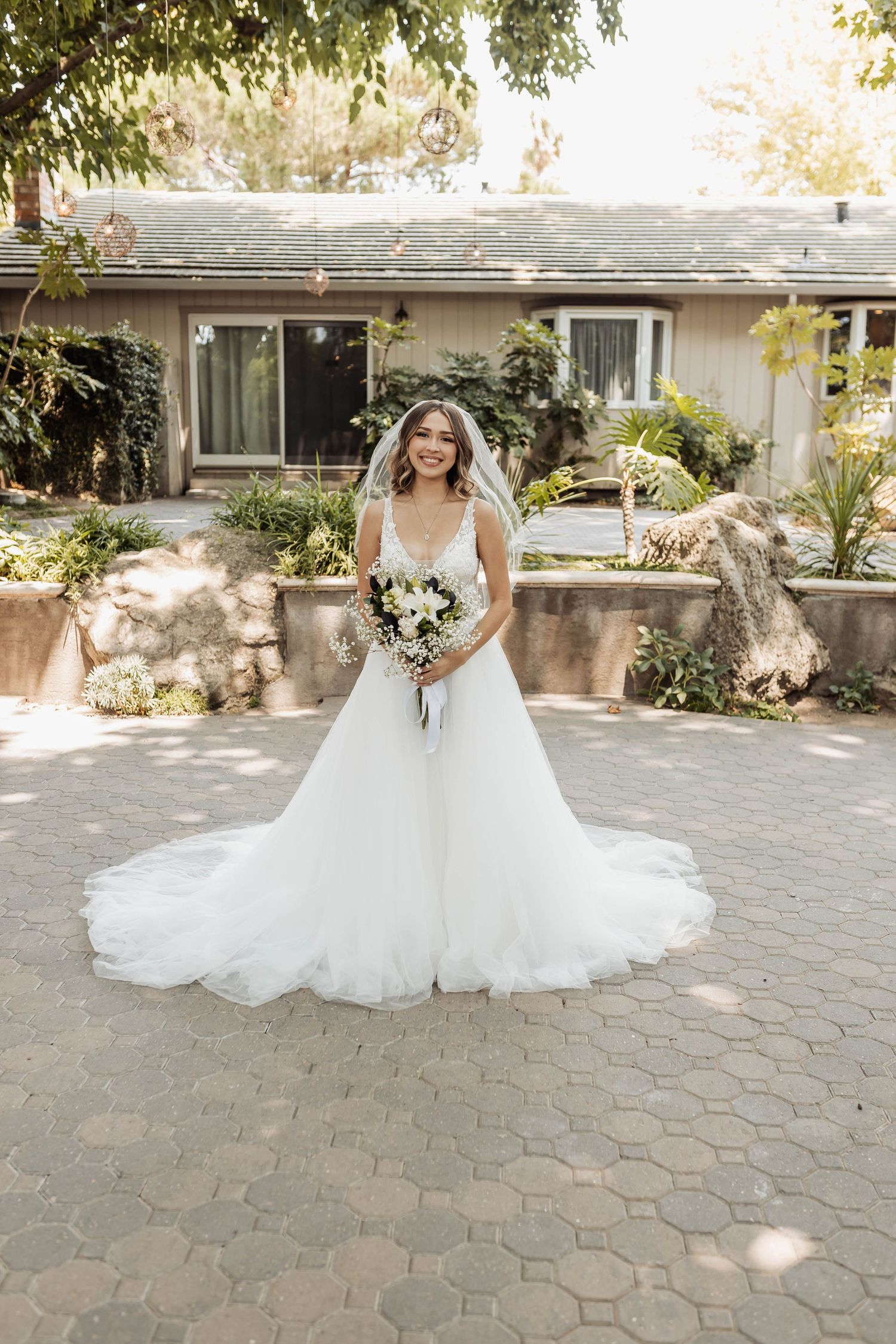 A stunning bridal portrait featuring a flowing white wedding gown on a stone paved courtyard in natural sunlight.