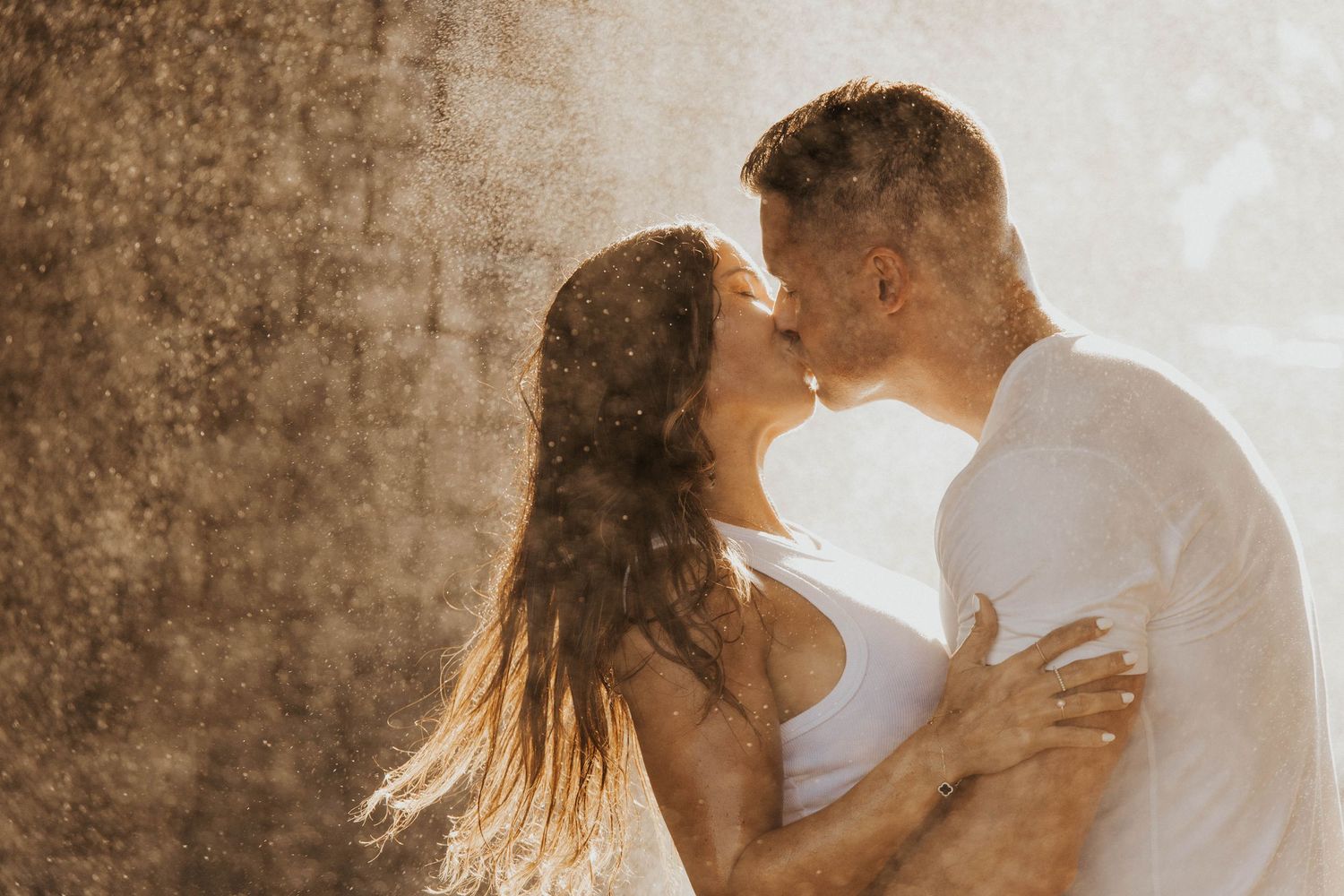 Intimate couple sharing tender moment against textured wall in golden sunlight.