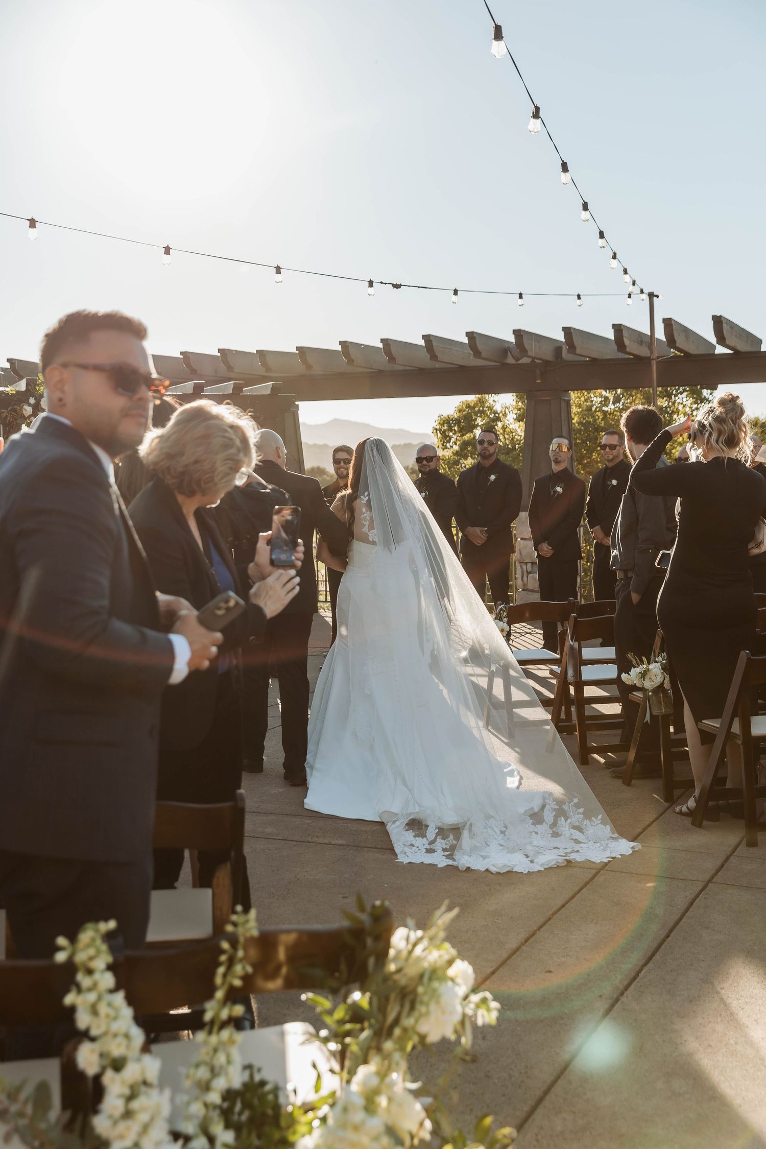 Couple shares their first dance at sunset during outdoor wedding ceremony with string lights overhead.