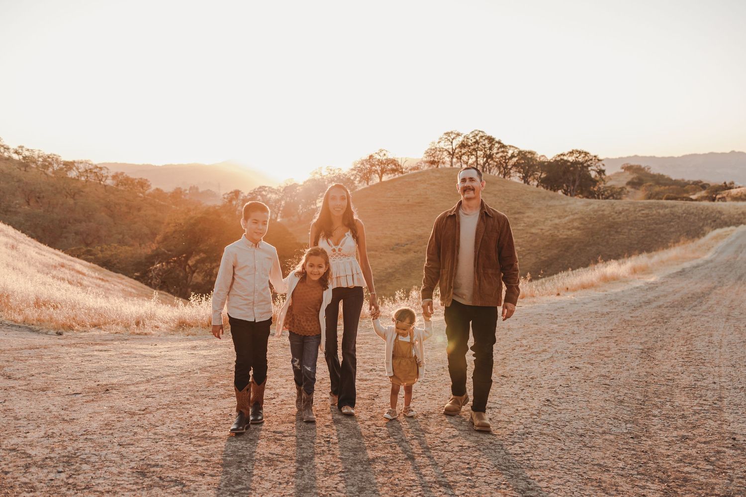 Silhouette of family walking together on hilltop trail during golden sunset.