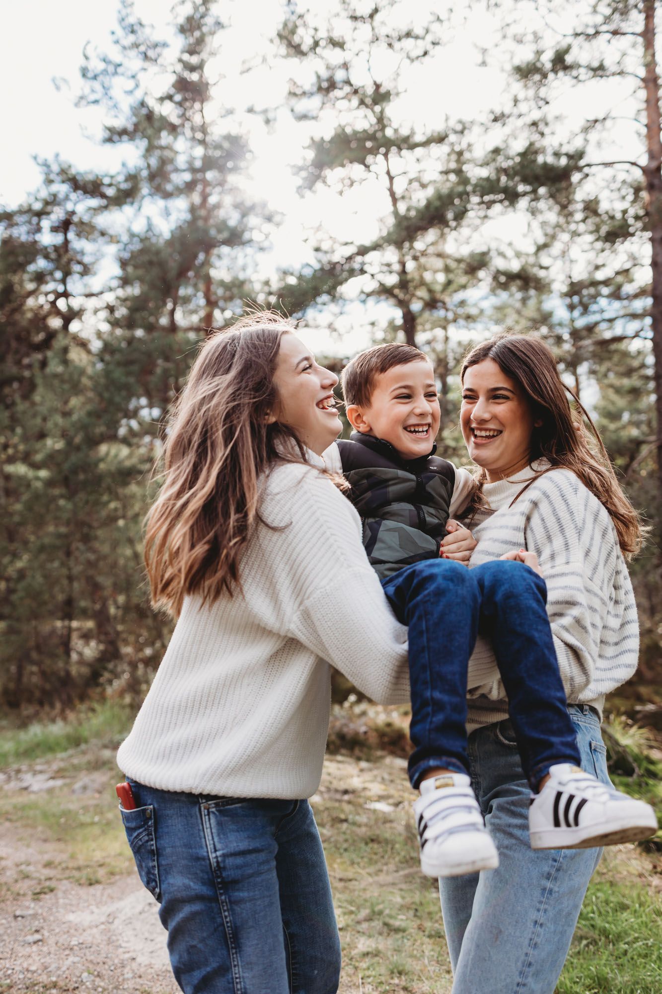 Three people share a lighthearted moment while playing together on a forest path.