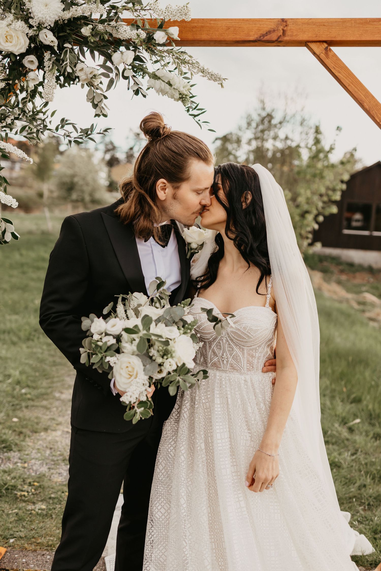 A romantic wedding moment captured under a floral arch in a garden setting.