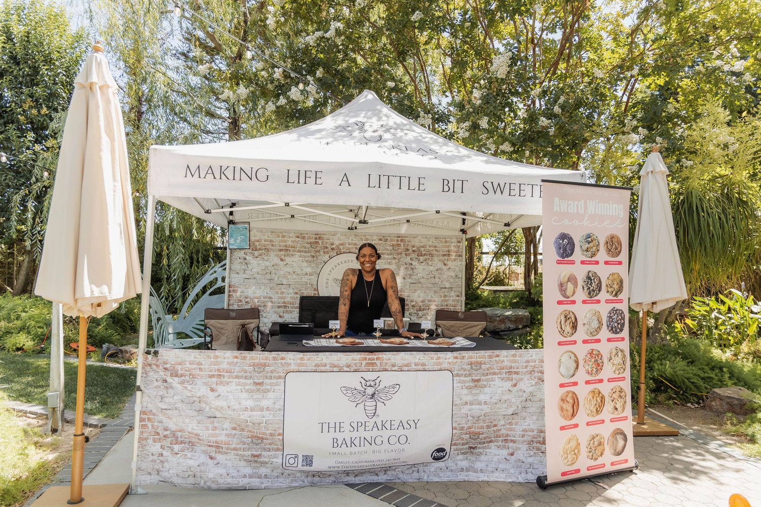 Woman at The Speakeasy Baking Co outdoor booth with sign reading Making Life A Little Bit Sweeter.