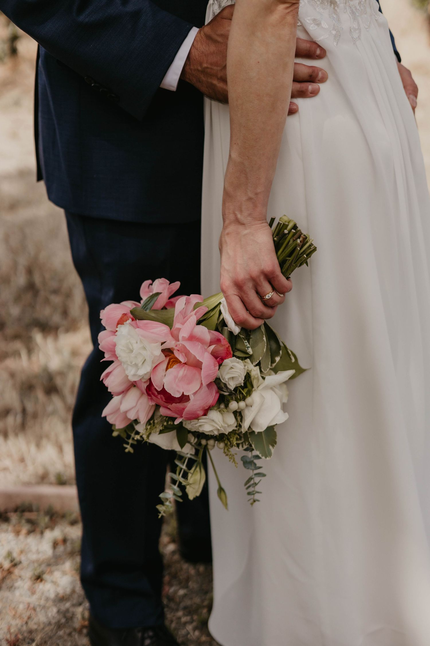 Close-up of couple holding pink and white wedding bouquet against formal attire.